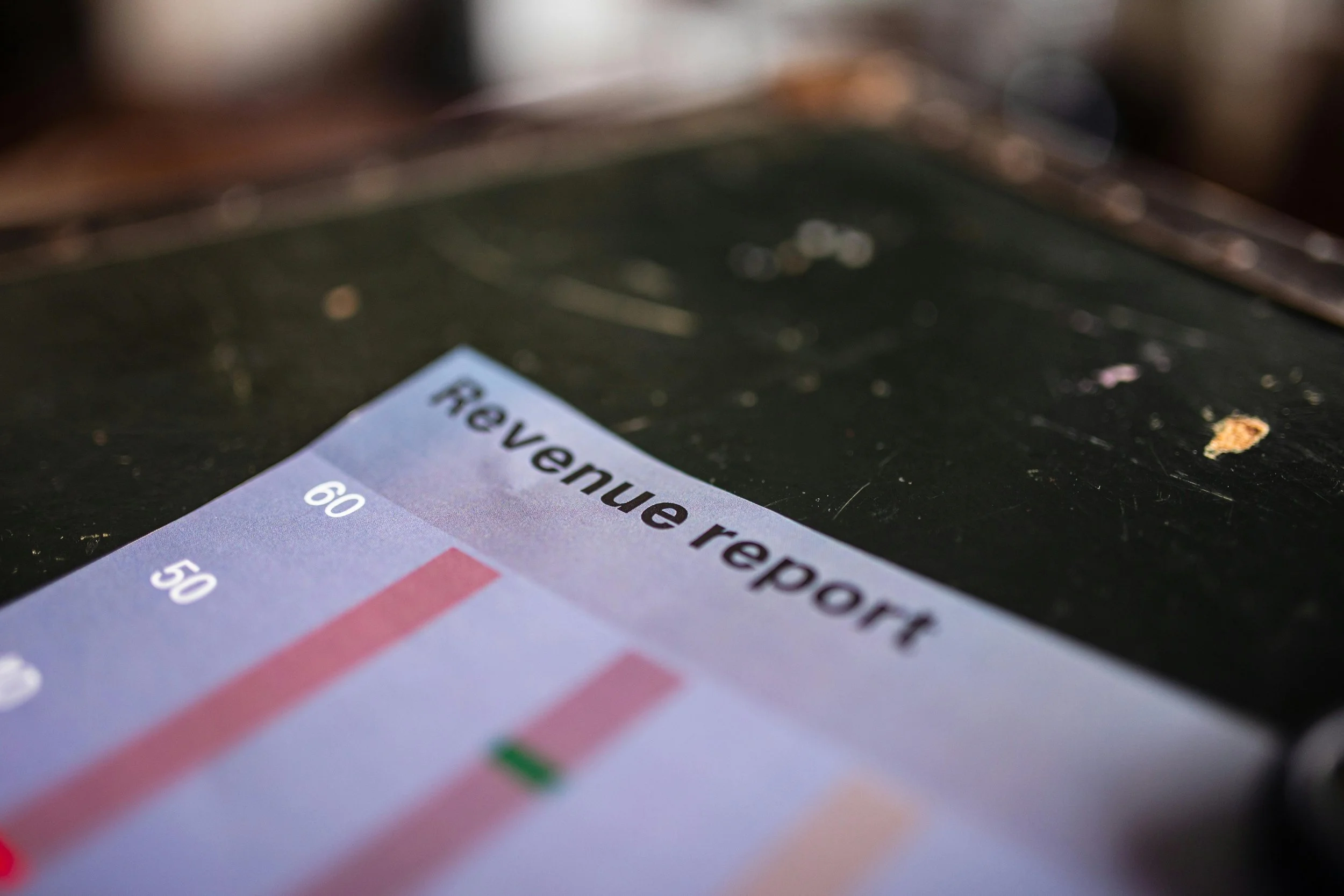 Close-up of a report or chart titled 'Revenu report' on a black surface, showing bar graph with red bars and some scratches or stains.