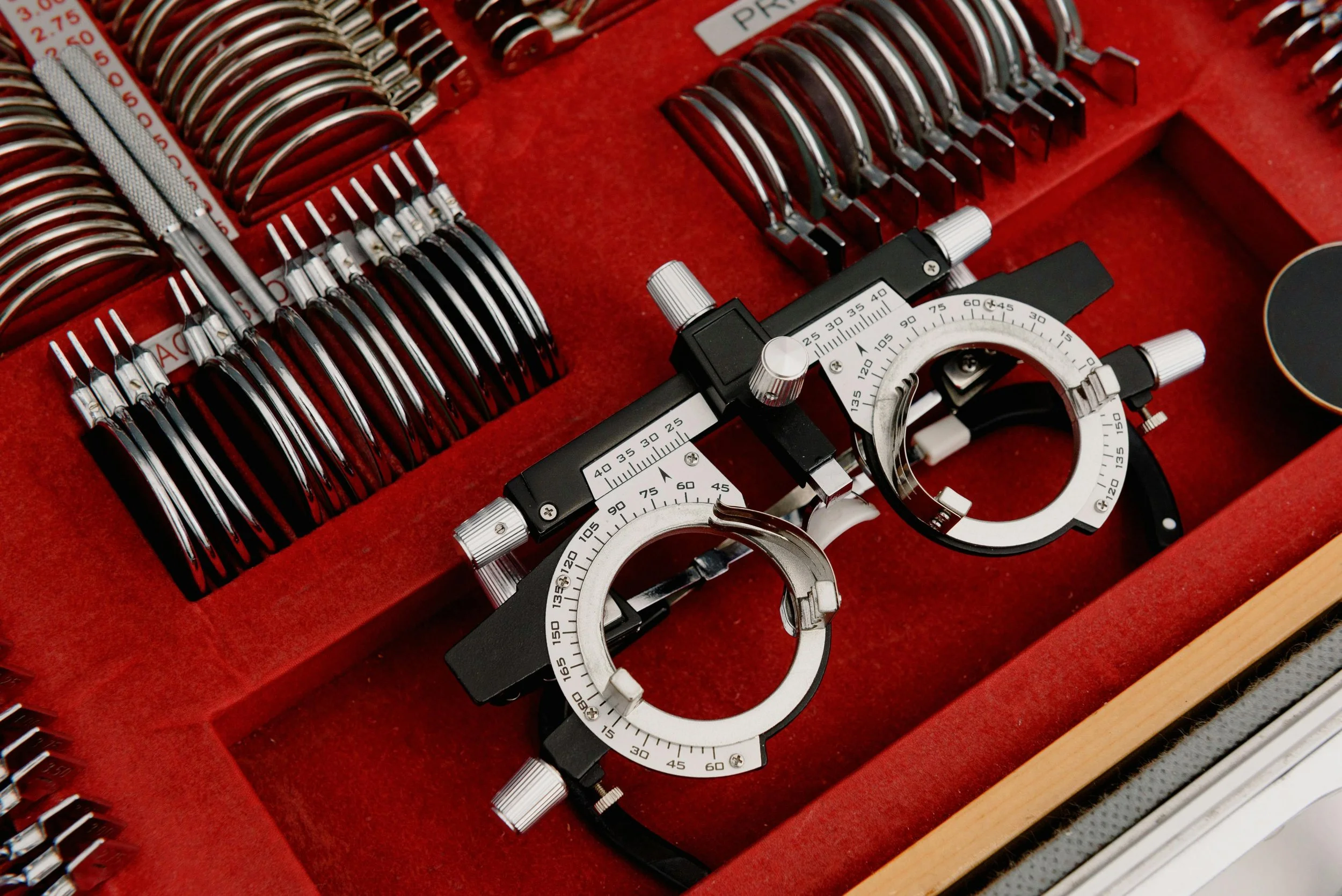 An eye examination phoropter with various lenses and an eye chart with red background.