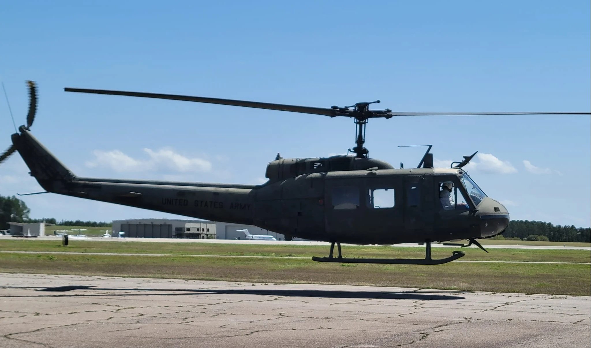 Military helicopter parked on airfield with blue sky and clouds in background.