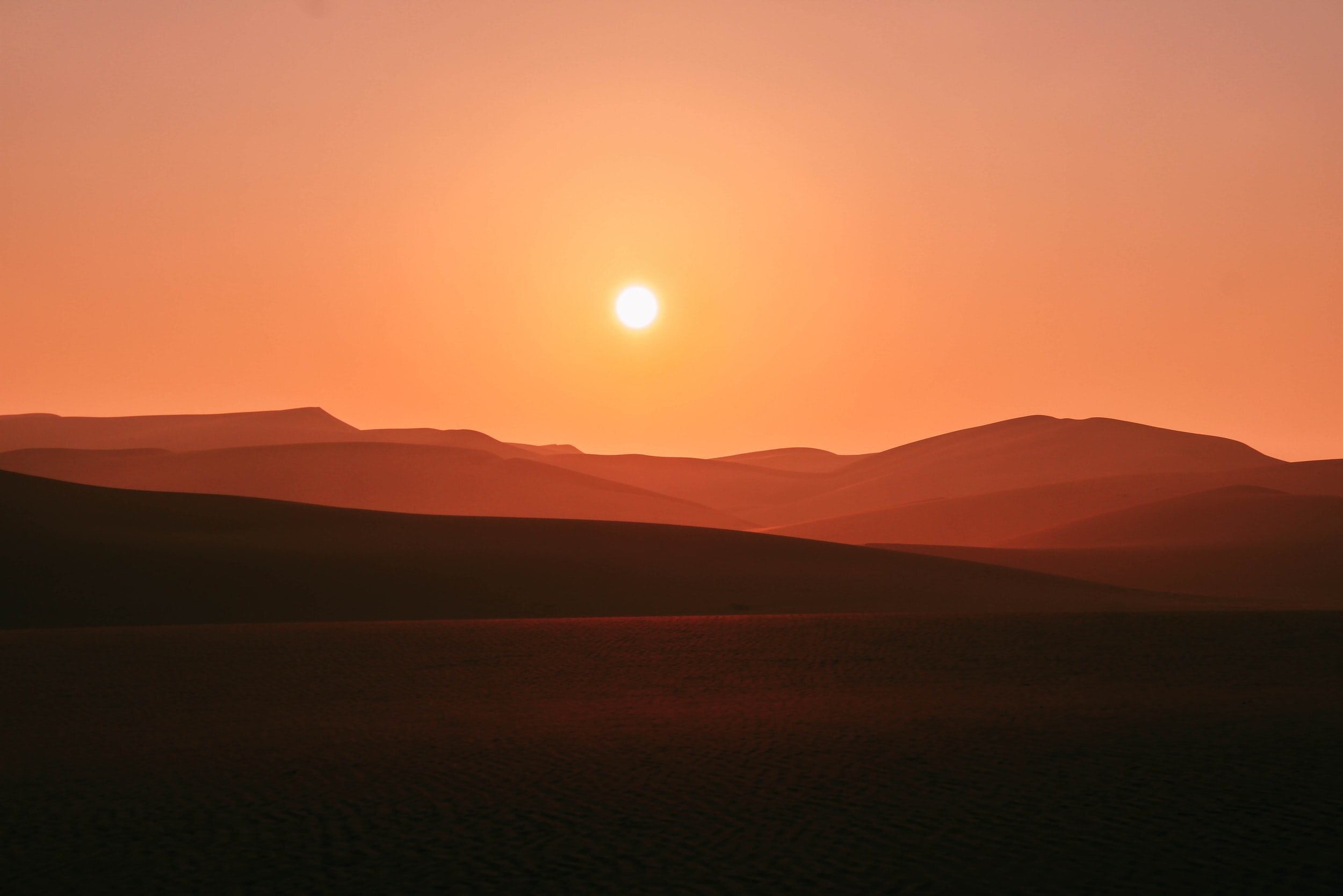 Image of orange sky with sun hanging low over hills.