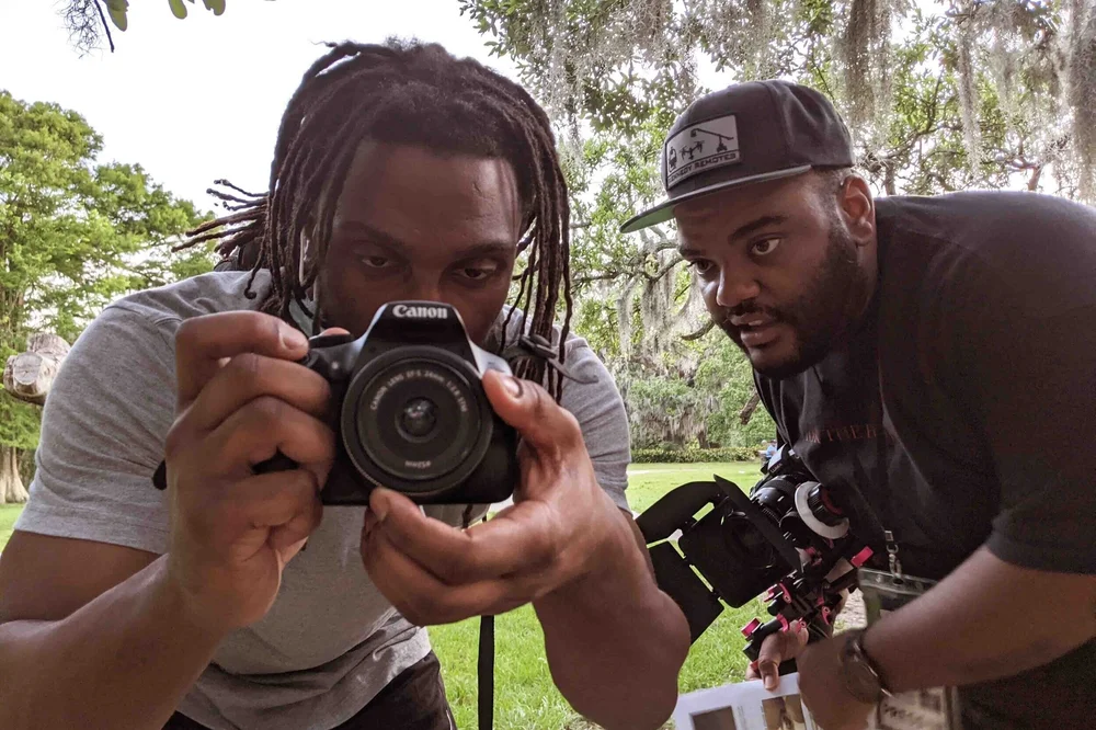 A fellow frames a shot with a camera while a mentor looks on