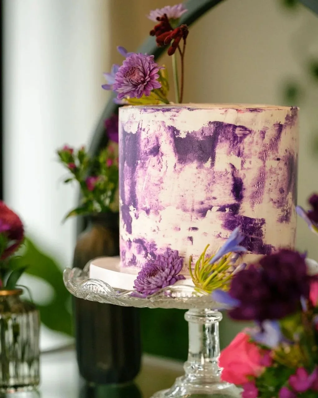   Creative Portland Oregon wedding cake with purple textured buttercream and floral accents displayed on a glass cake stand.  