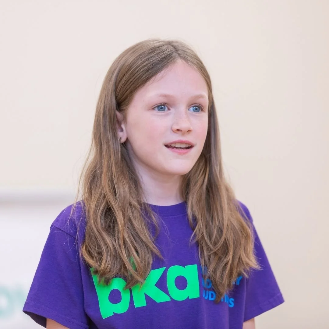 A young girl in a purple Broadway Kids Auditions t-shirt practices her vocal performance during a workshop.