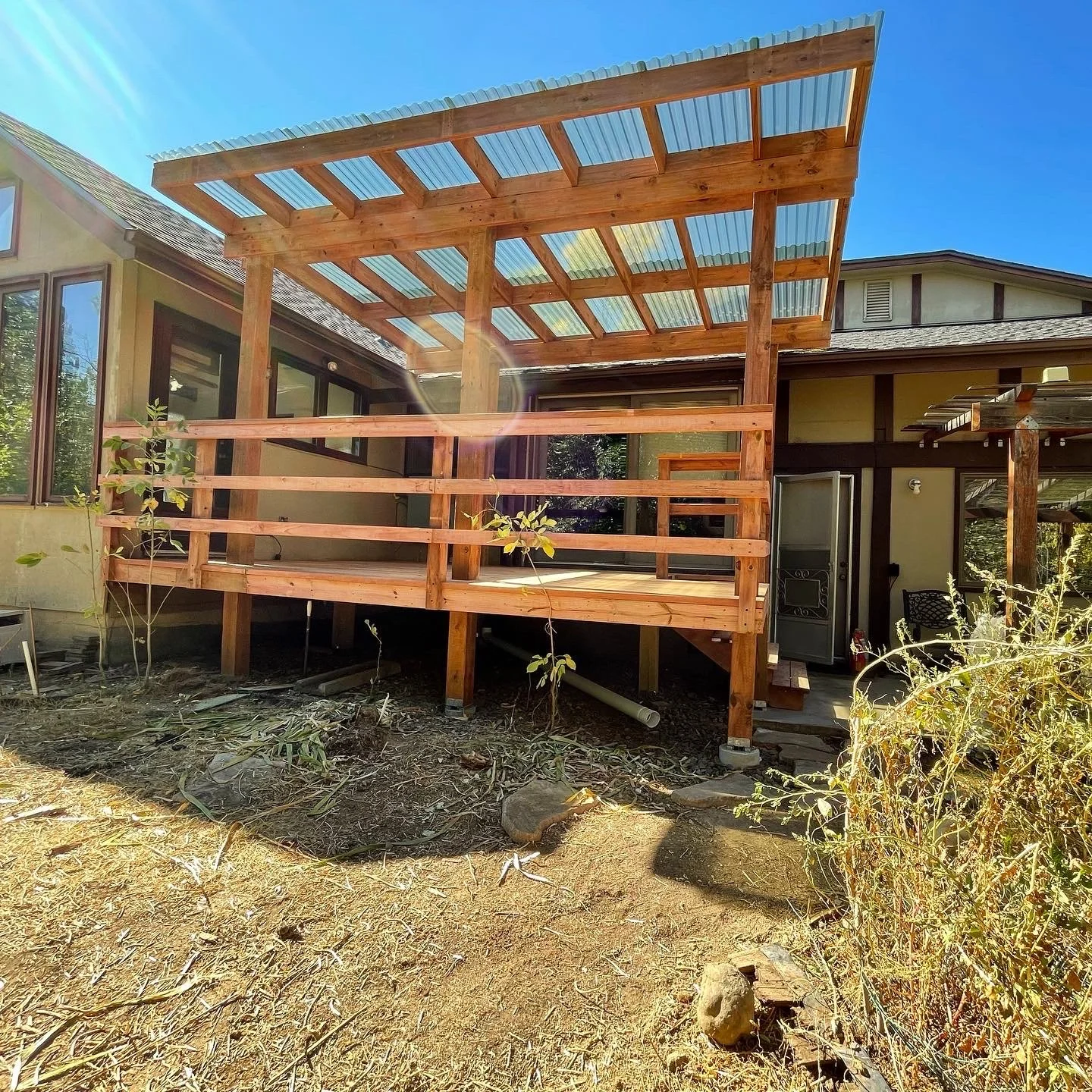 Wooden raised deck with a translucent corrugated patio roof attached to a house. Otto Custom Builders provides residential construction, exterior home improvements, and remodeling services in Denver, Aurora, Lakewood, Centennial, Littleton, Parker.