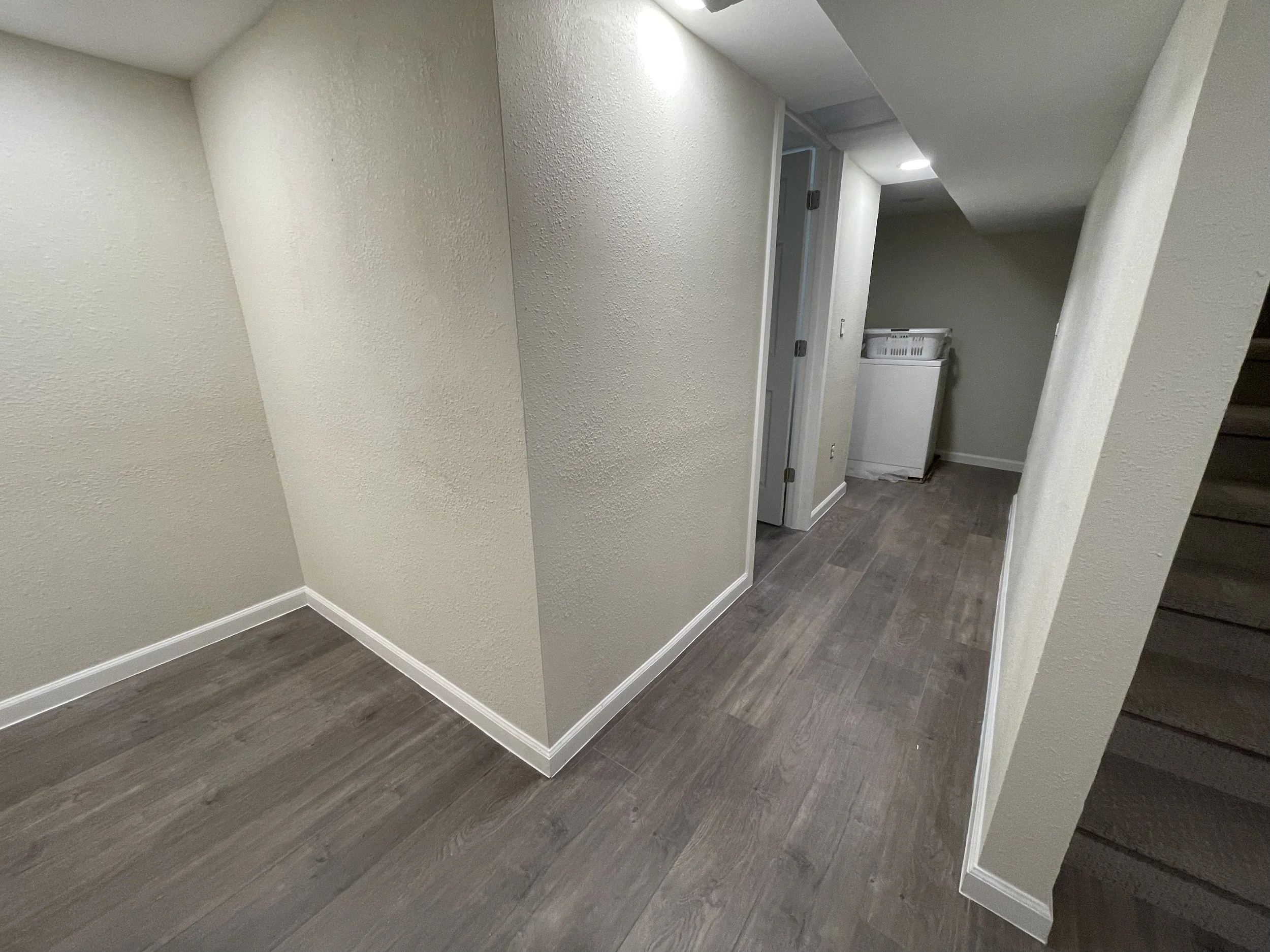 Interior remodeling by Otto Custom Builders featuring gray wood-look flooring, textured walls, carpeted stairs, and a laundry area with a washer. Professional flooring installation, interior renovations, and home improvement services in Denver Aurora