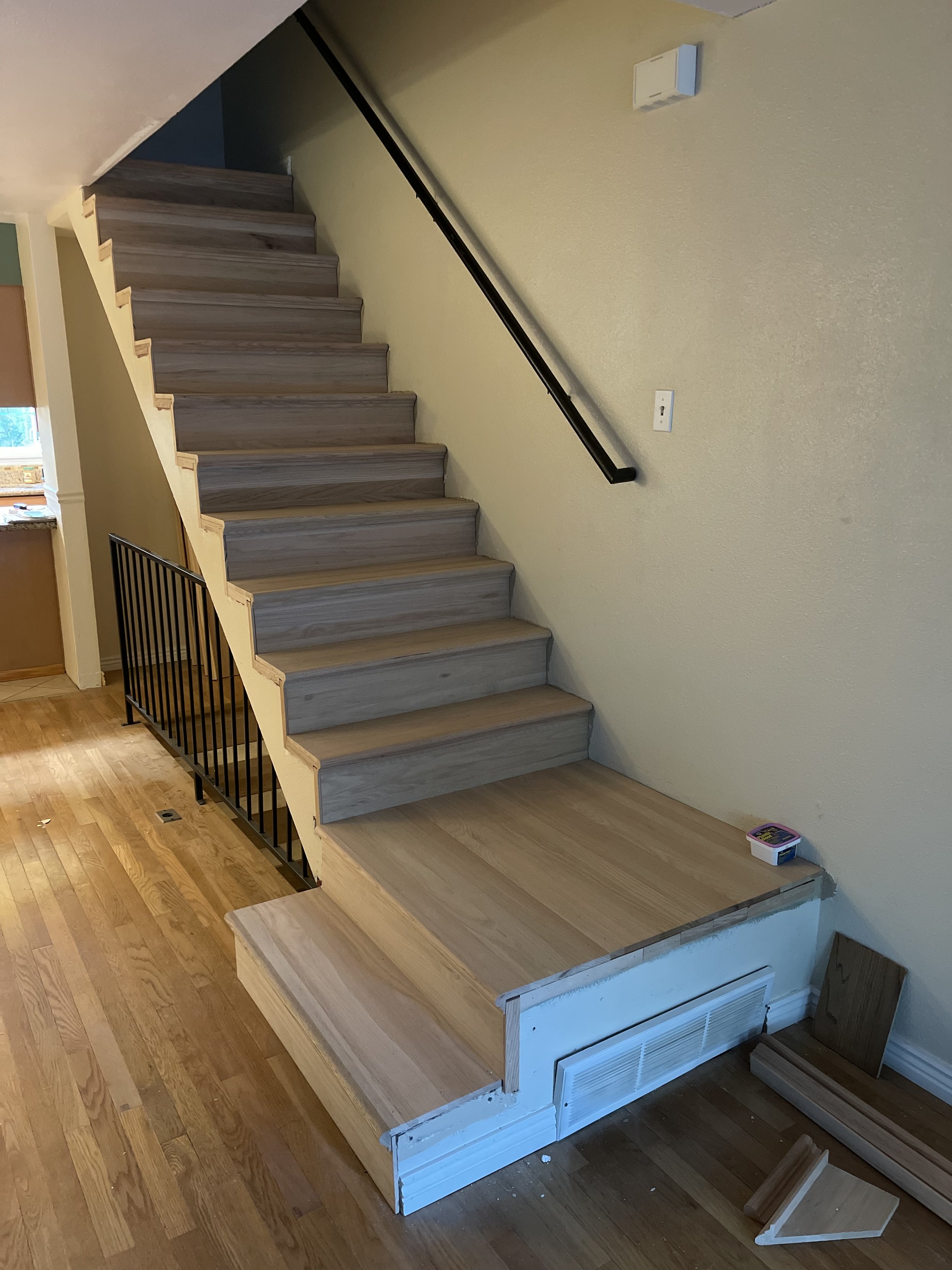 Interior staircase remodeling by Otto Custom Builders featuring gray wood-look stair treads, a black handrail, a safety gate, and hardwood flooring. Professional stair renovations, flooring installation, and interior remodeling services in Denver.