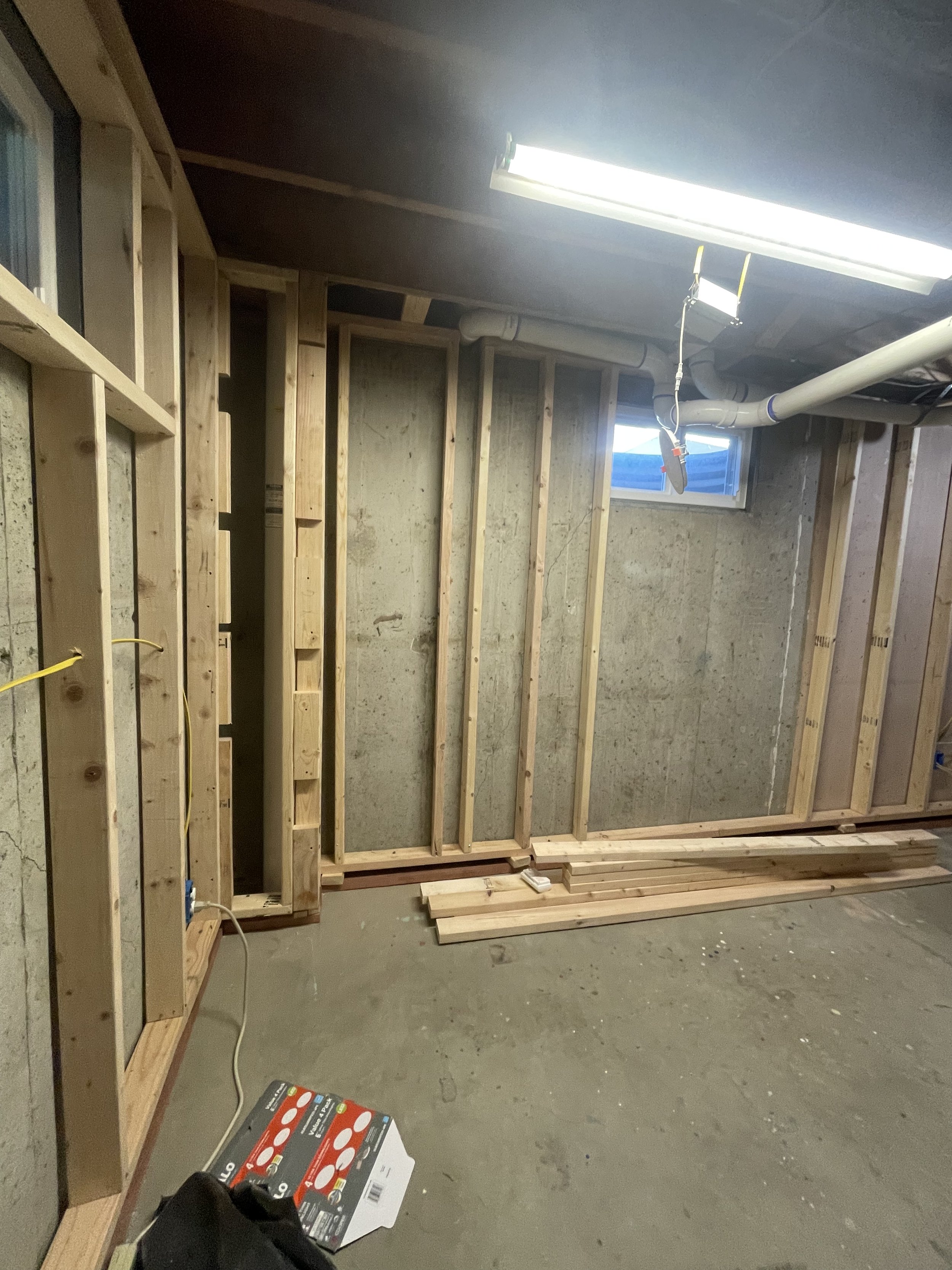 Unfinished basement renovation by Otto Custom Builders featuring exposed wall studs, concrete foundation walls, plumbing pipes, electrical wiring, and construction lumber. Professional basement remodeling, framing, and home renovation services.