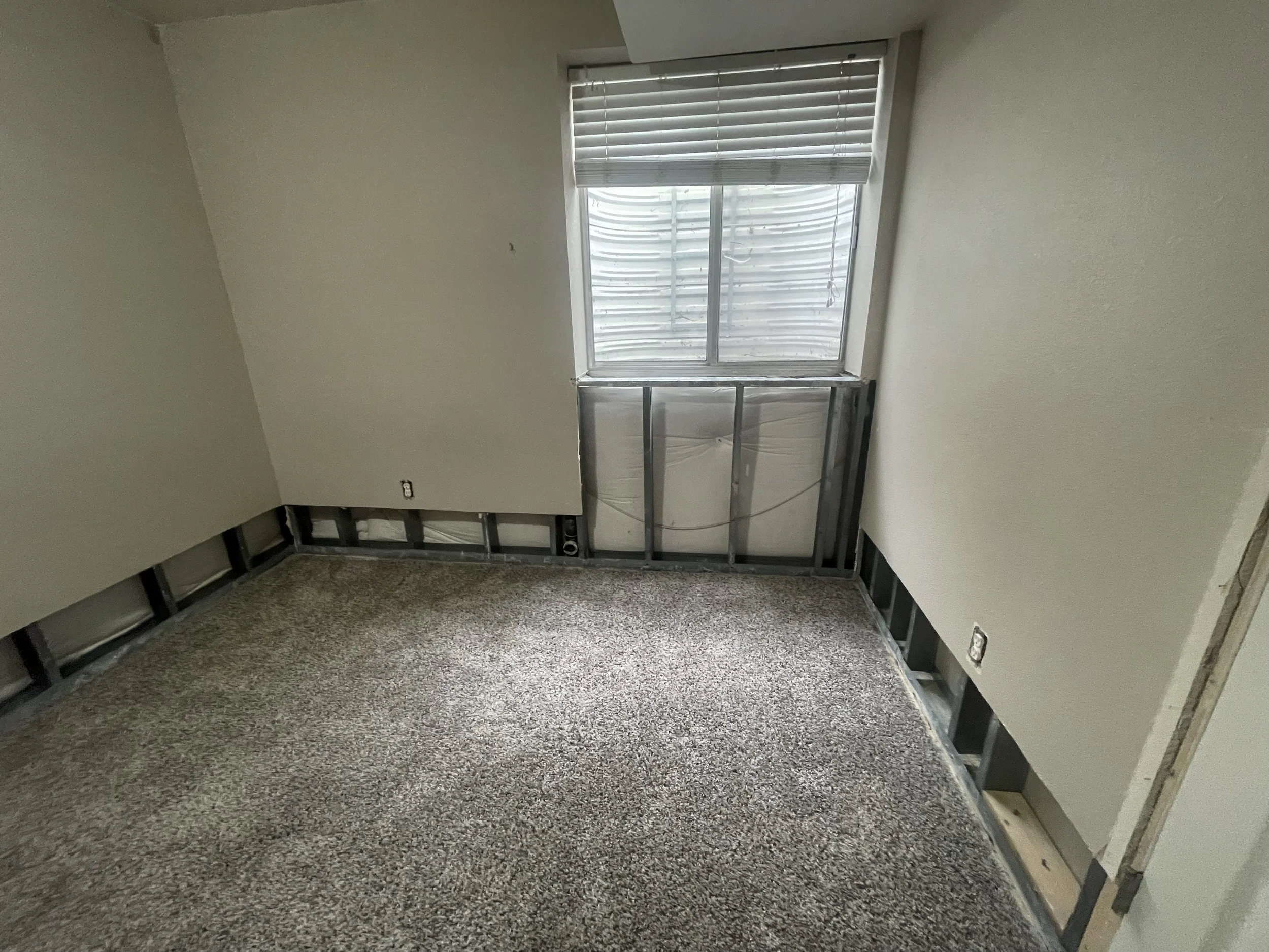 Unfinished room remodeling by Otto Custom Builders featuring exposed wall framing, insulation, electrical outlets, and a window with blinds. Residential framing, drywall installation, and interior renovation services in Denver, Aurora, Centennial.