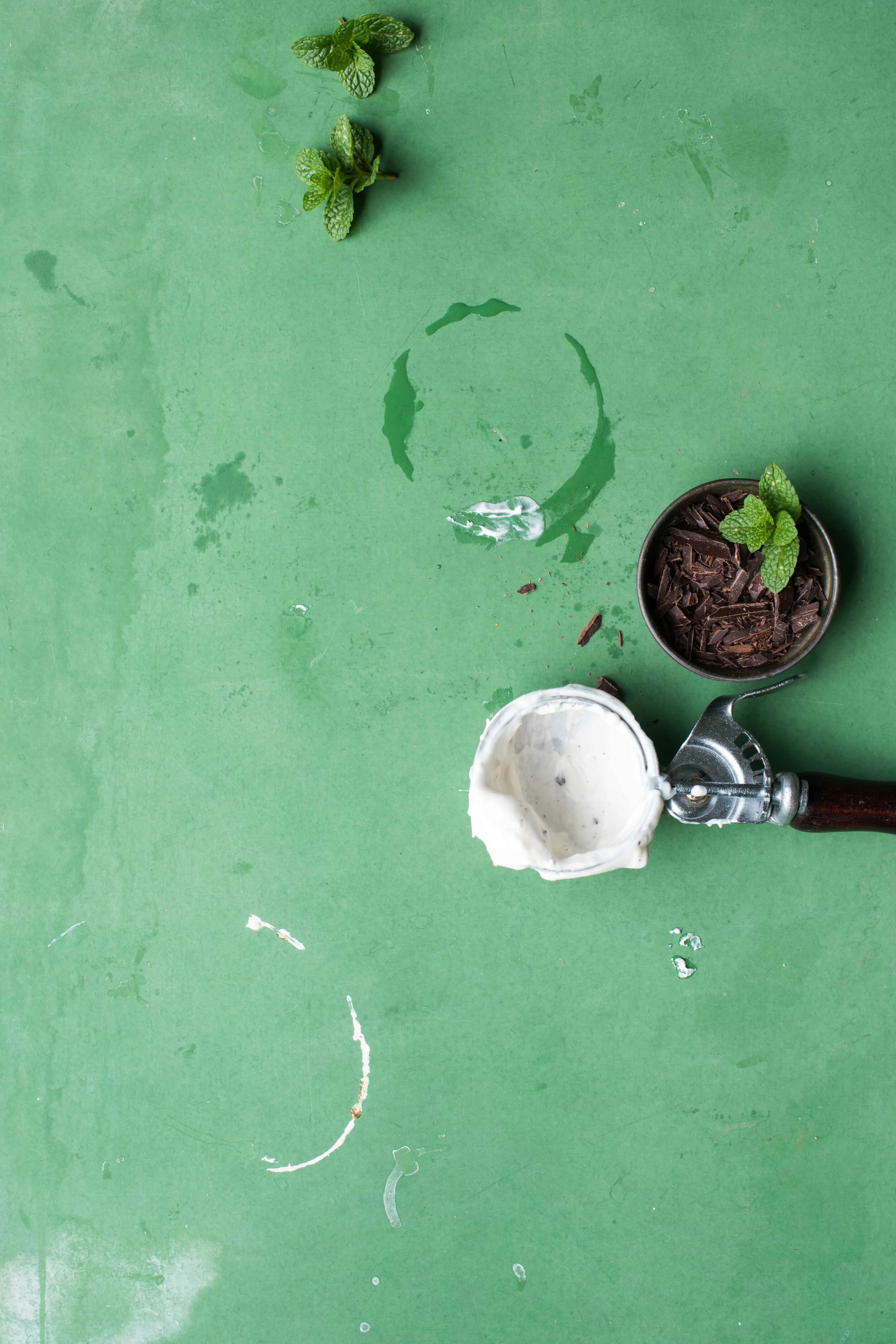 An ice cream scoop. Mint sprigs, chopped chocolate. Shot on a green background.