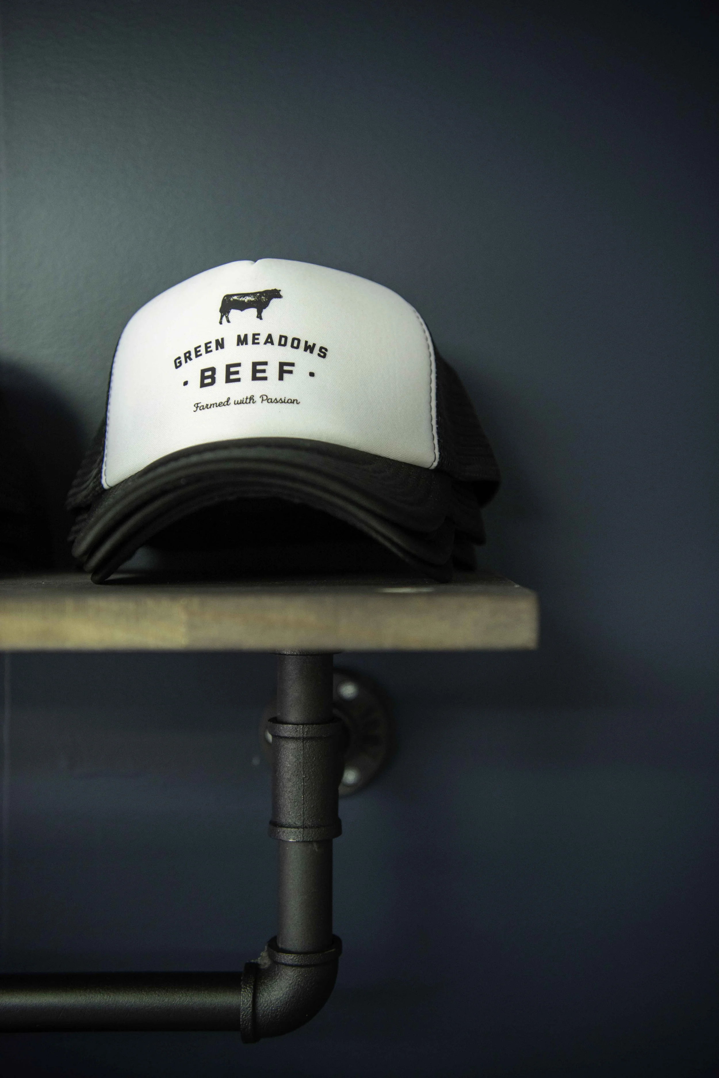 Stack of Green Meadow’s Beef Truckers hats on a shelf shot on a dark background.