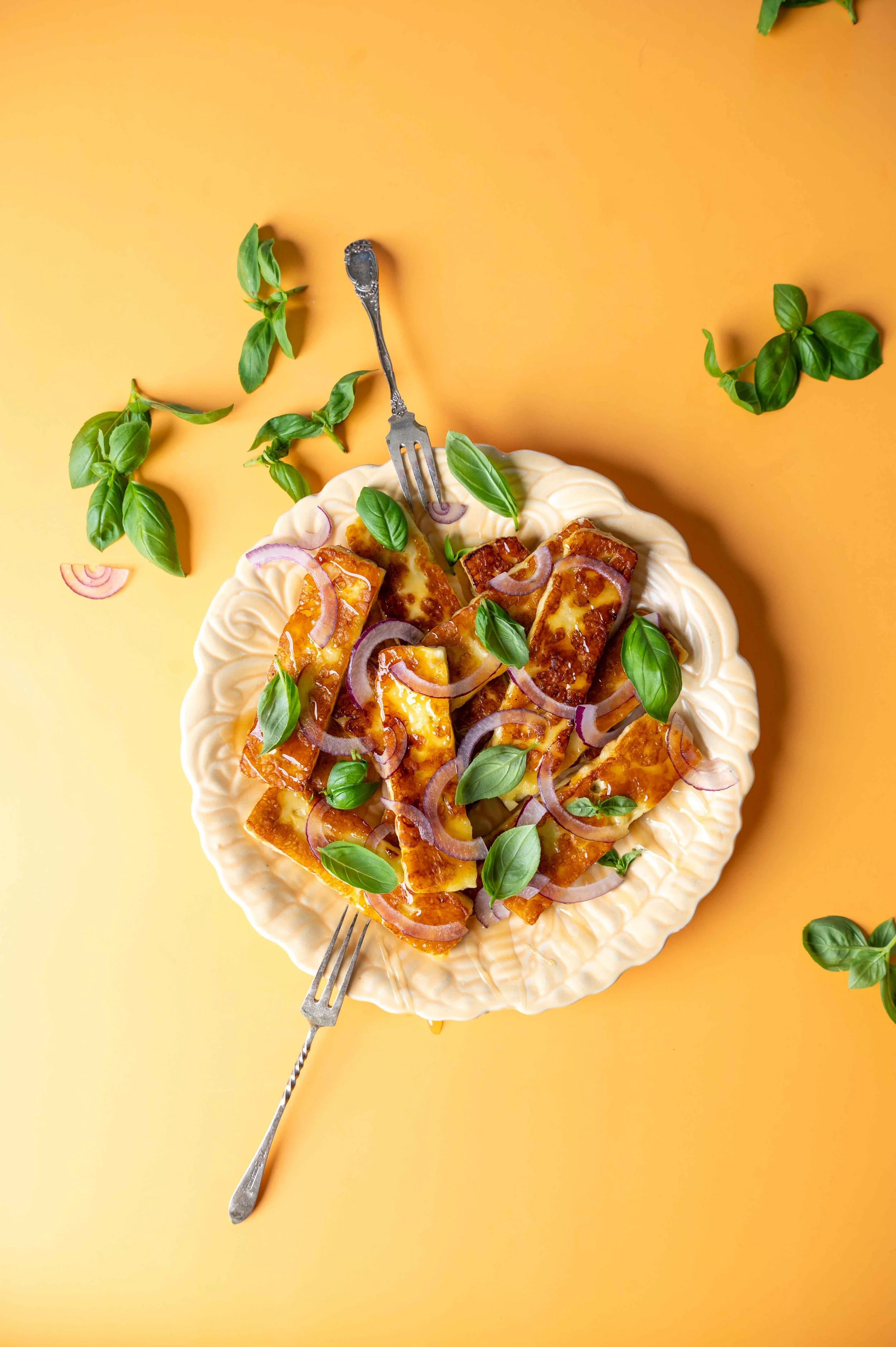 Fried Hamoumi for Egmont Honey shot on a decorative plate, seen from above, on a yellow background with scattered basil leaves.
