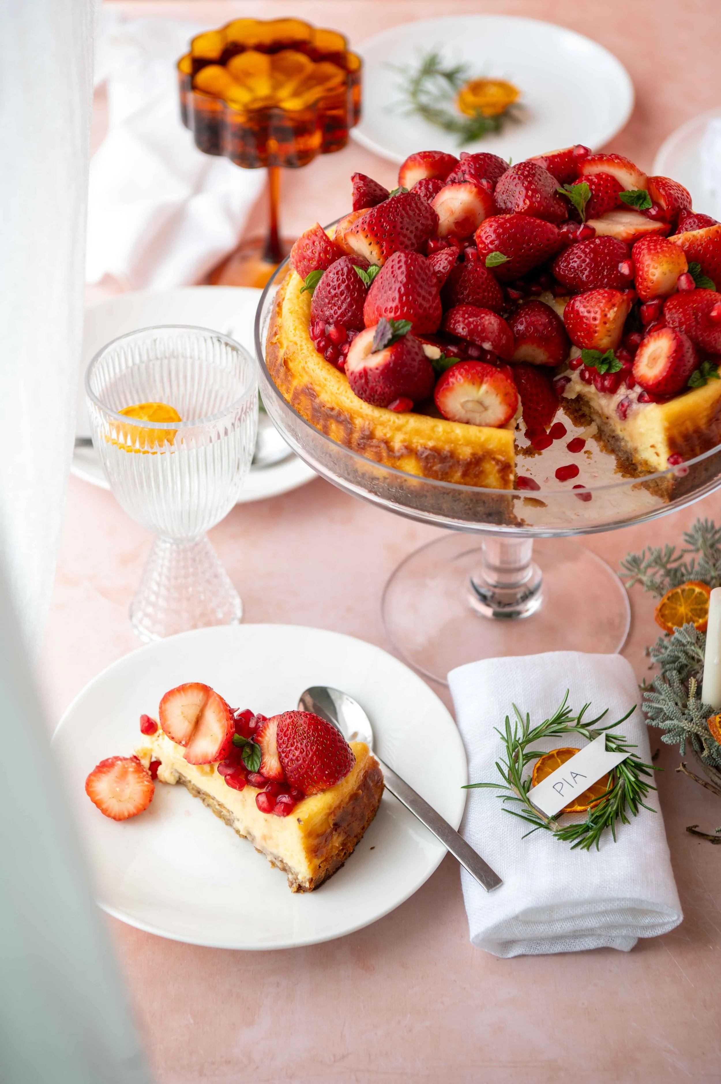 Strawberry Cheese piled high with strawberries. A slice on a plate. A glass of water and a napkin with the name tag ‘Pia”.