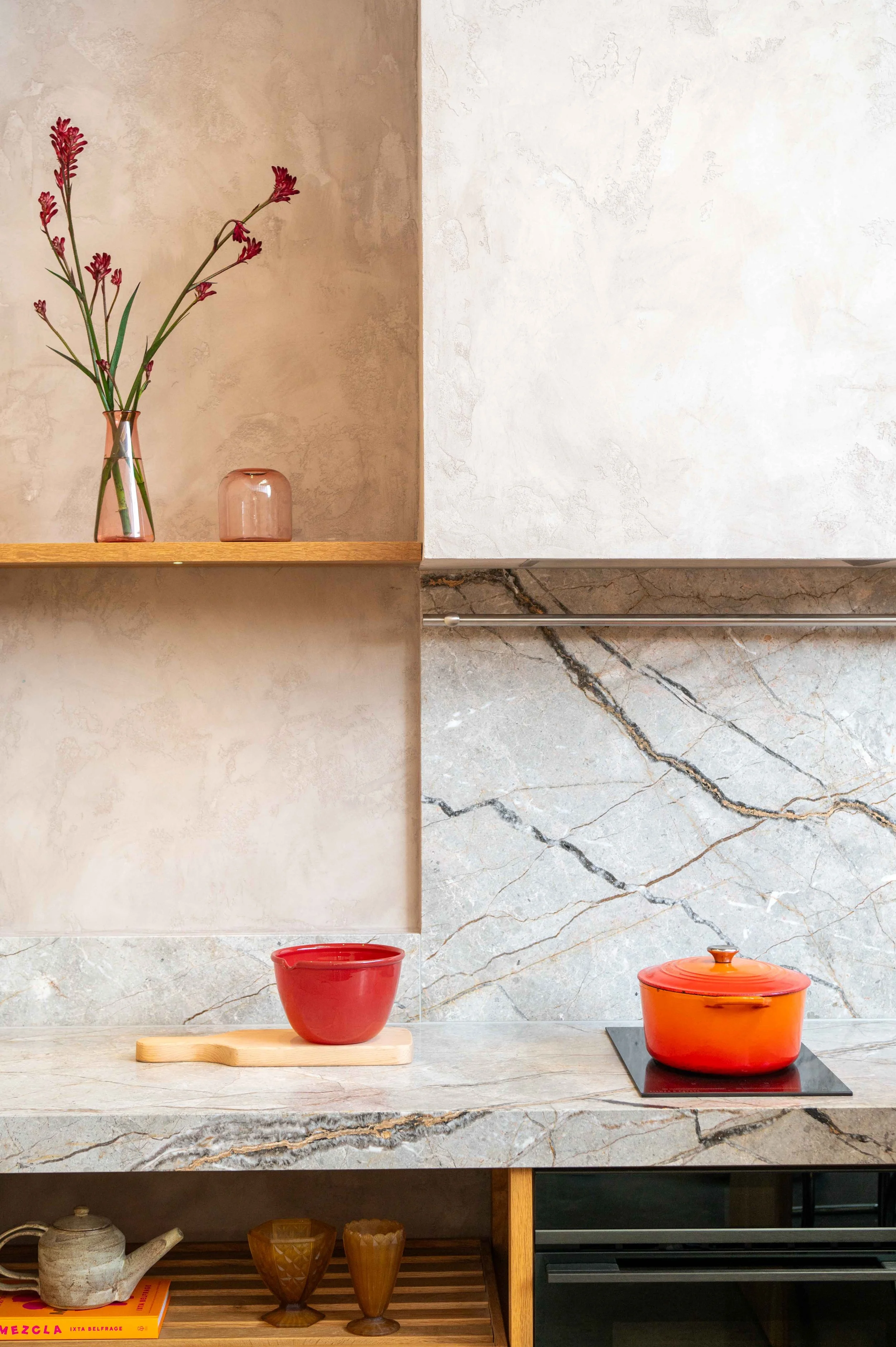 A modern modular kitchen with marble countertop and splash back. Natural light. Styled with red and pink props.