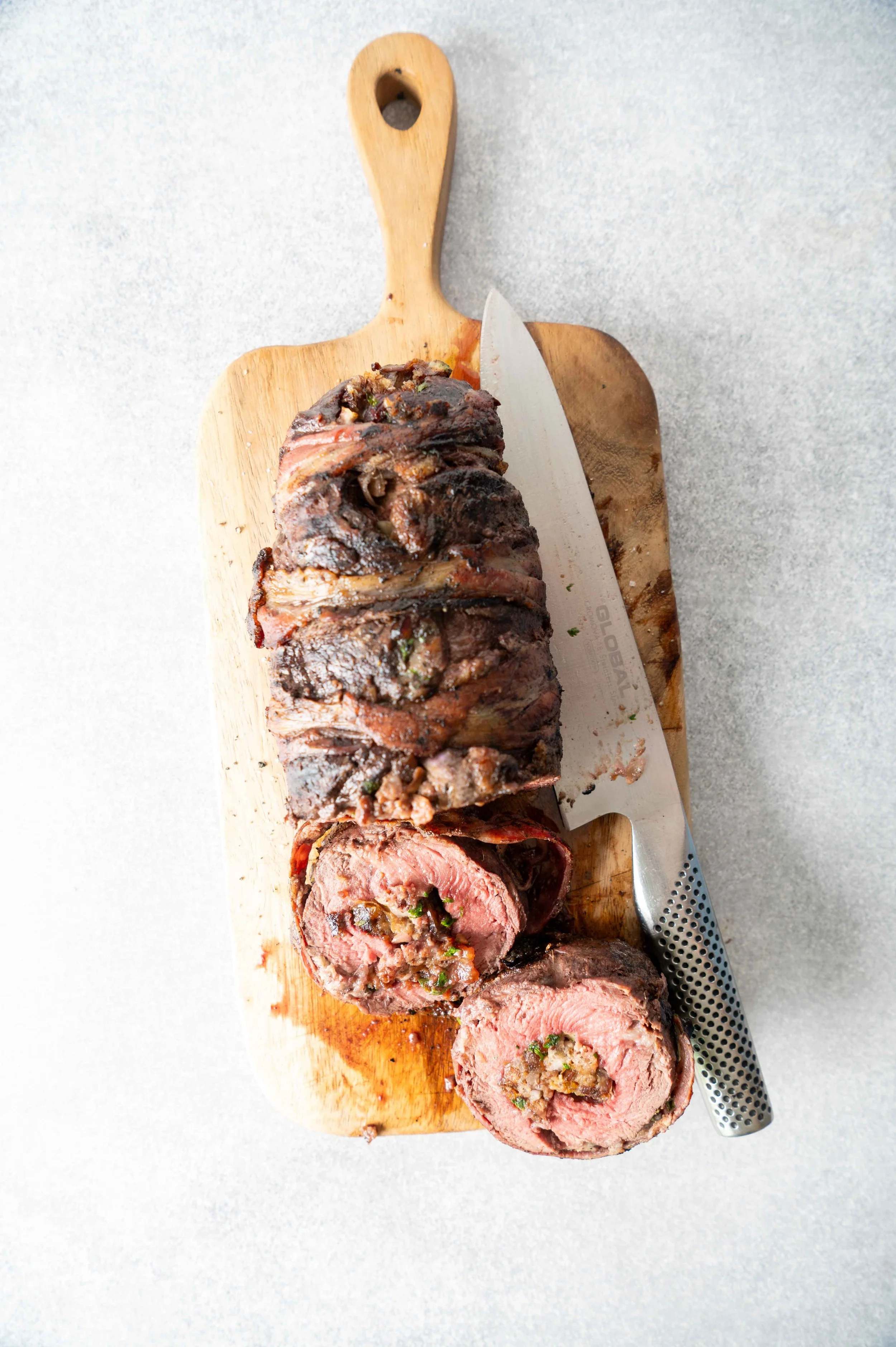 Cooked beef tenderloin roast sliced on a wooden cutting board with a chef's knife.