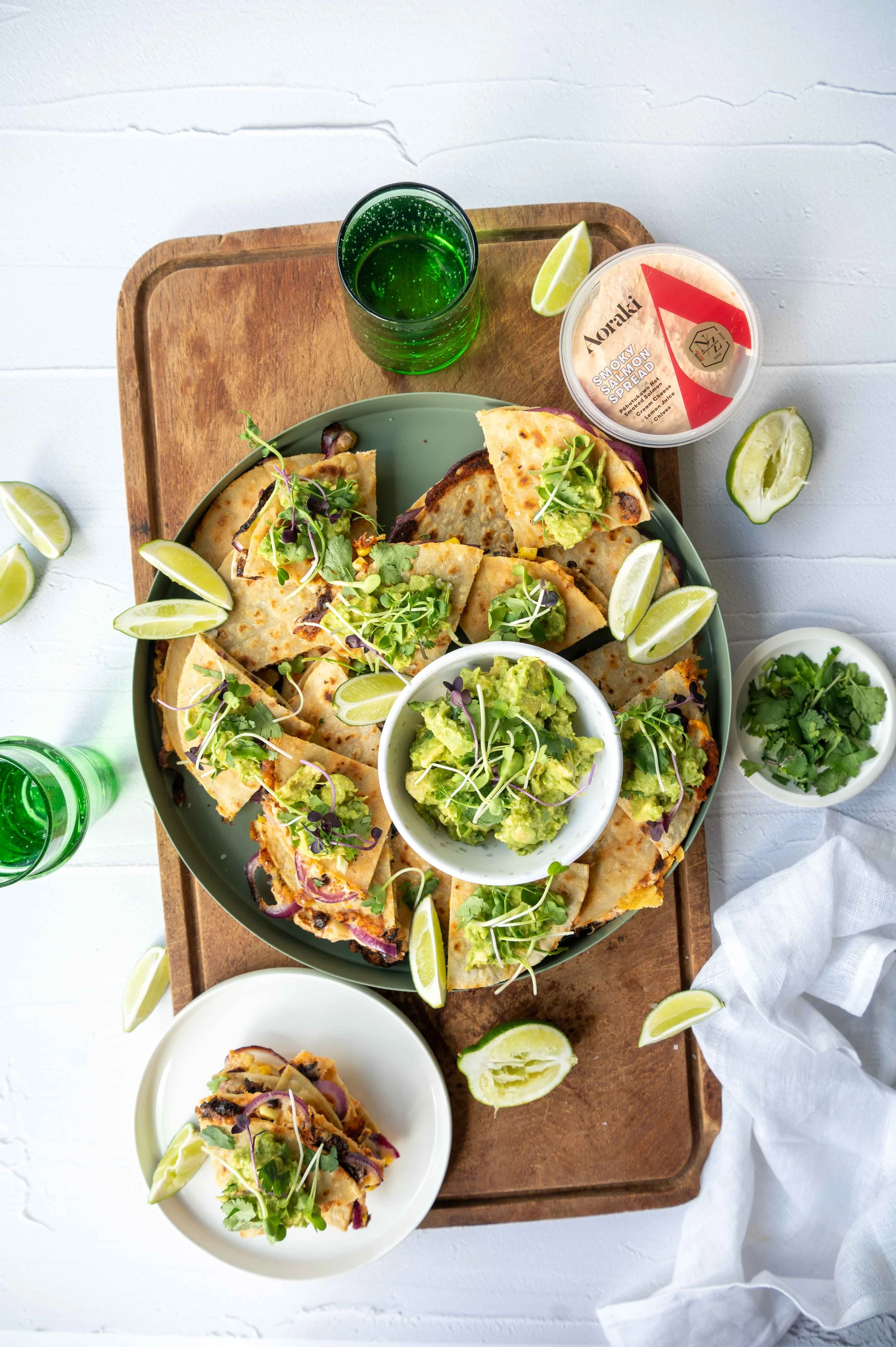 Aoraki Salmon Smoked Salmon Quesadillas. Smoked salmon spread sits on a wooden board with a tray of quesadillas and a single serve on a white plate.