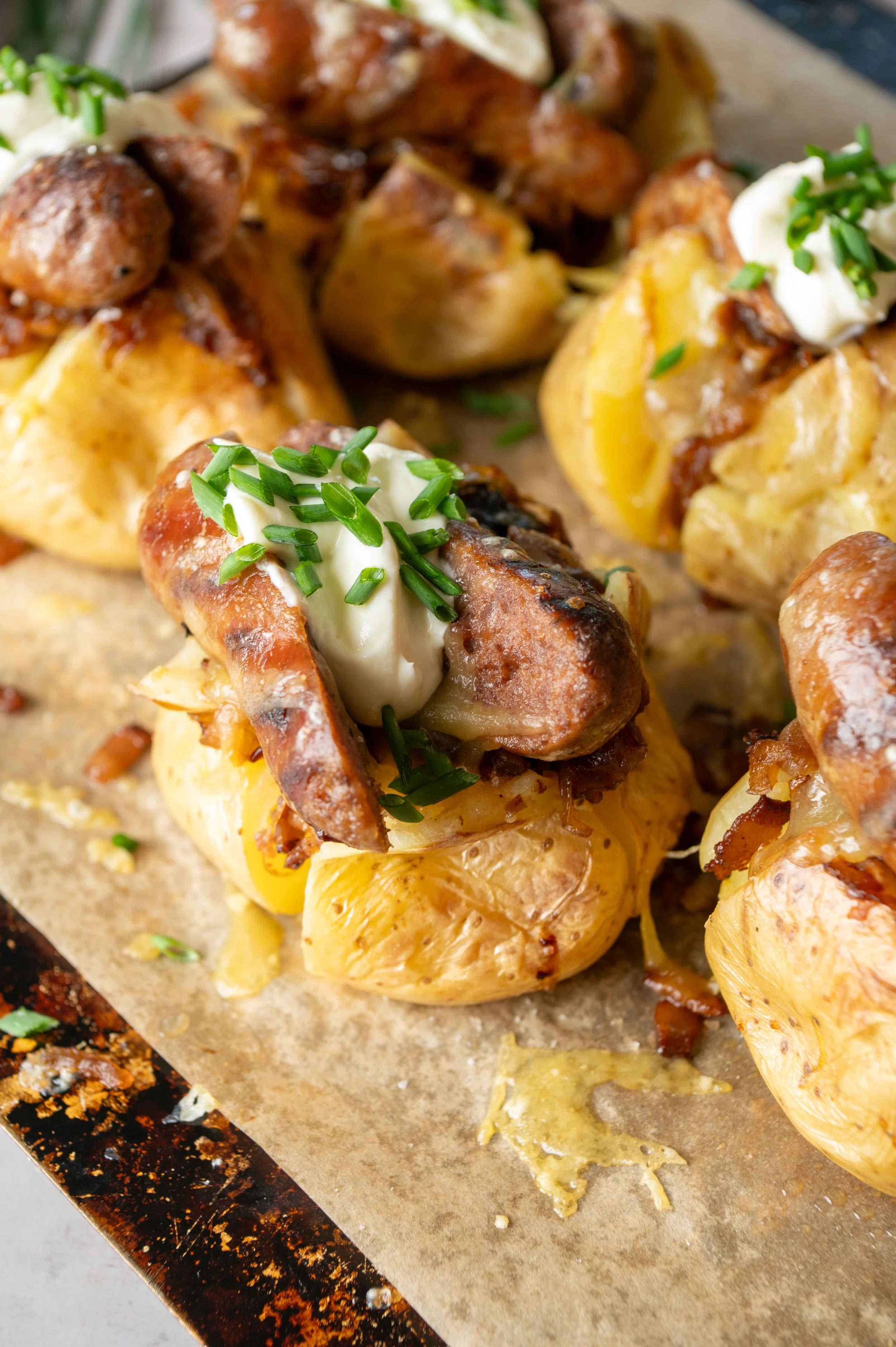 Loaded baked potatoes topped with sour cream, chopped chives, shredded cheese, bacon bits, and cooked sausage.
