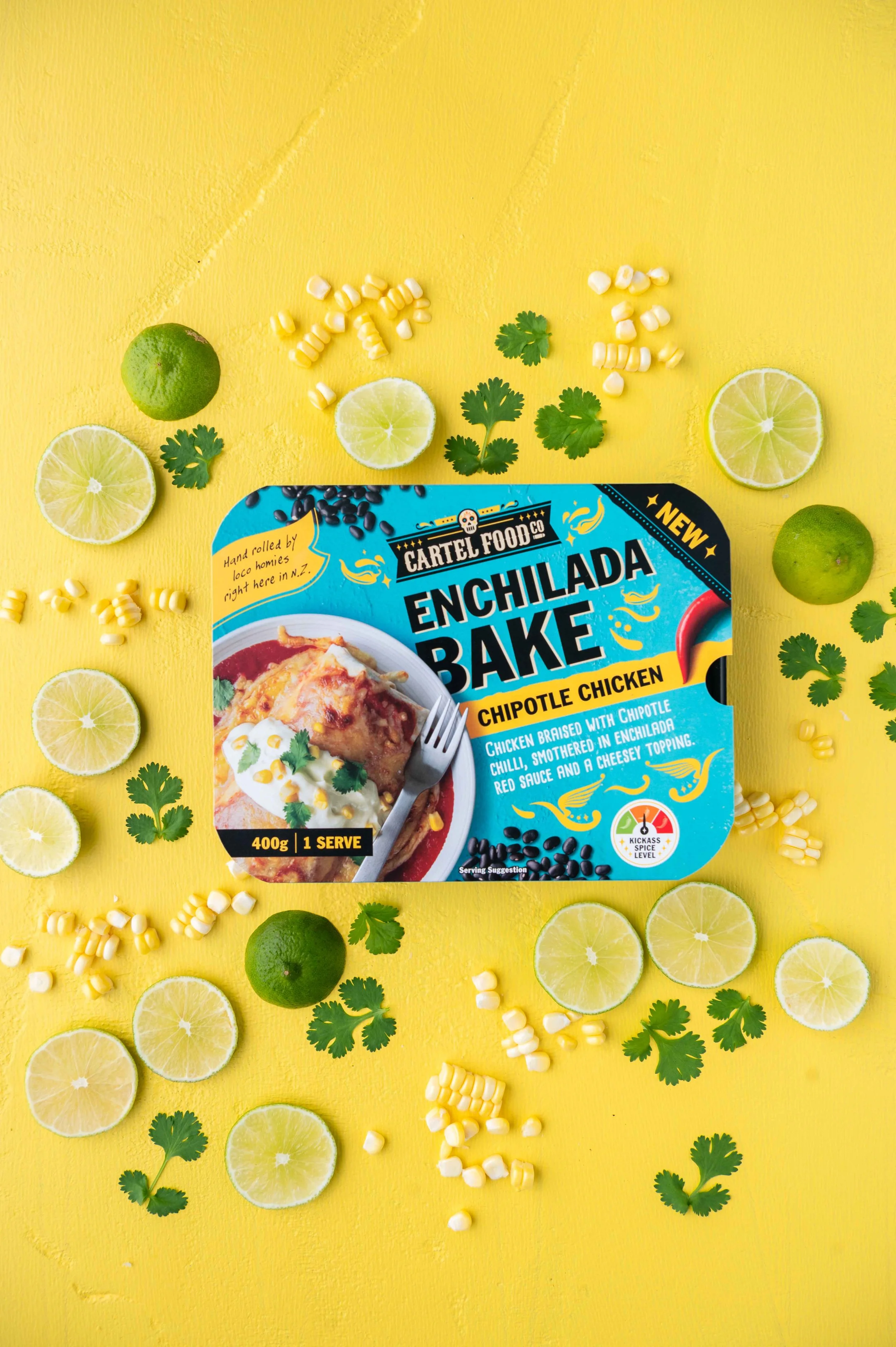 Package of Cartel Food Co Enchilada Bake Chipotle Chicken surrounded by lime slices, corn, and cilantro on a yellow background.