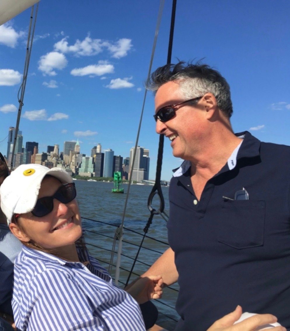 Smiling couple on a sailboat with a city skyline behind them