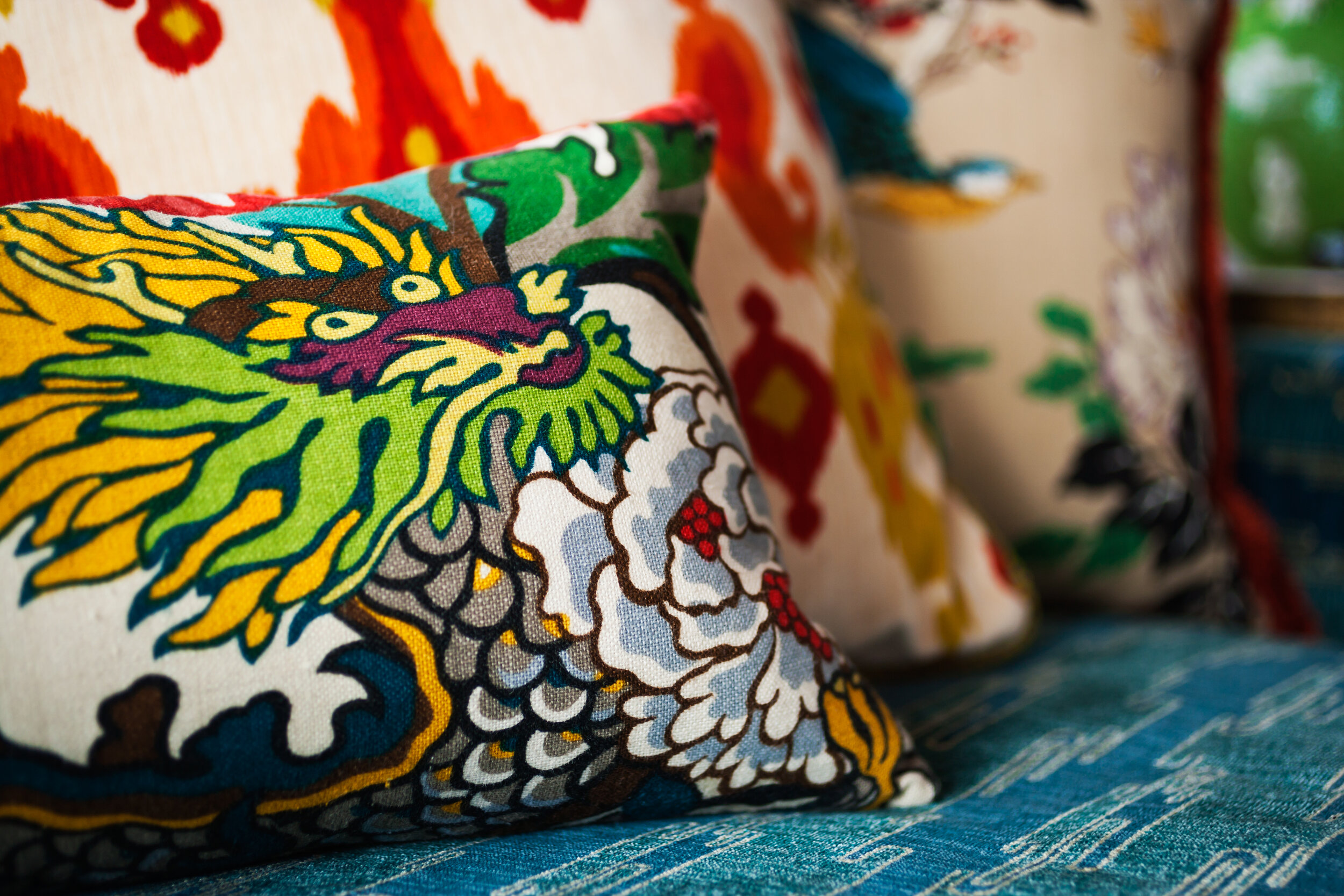 Colorful, embroidered decorative pillows with floral and abstract patterns on a blue textured surface.