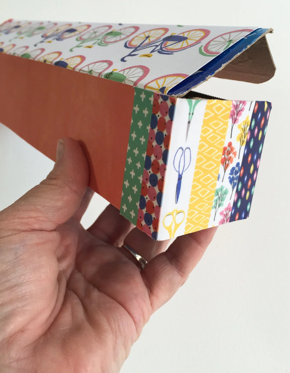 Once you get the entire outside of the box covered, cut a piece of coordinating paper for the inside of the box. It is important to score the folds for the inside as the box top can begin to get stiff with the layers of paper over the cardboard. Lig…