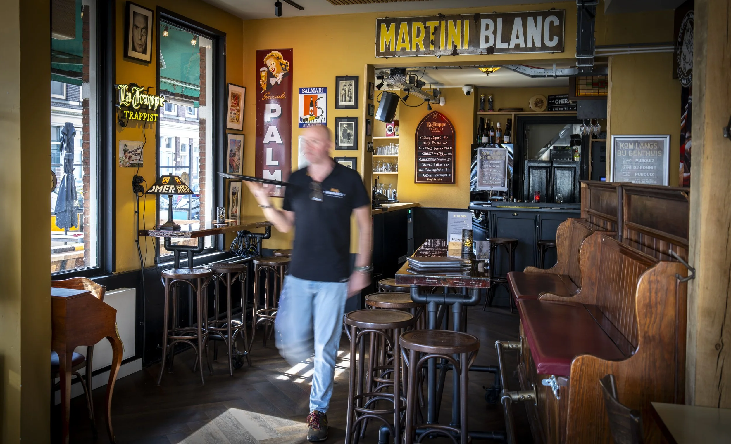 Binnen in een bar of café met gele en donkere muren, met een man die een dienblad vasthoudt, door de kamer lopen.