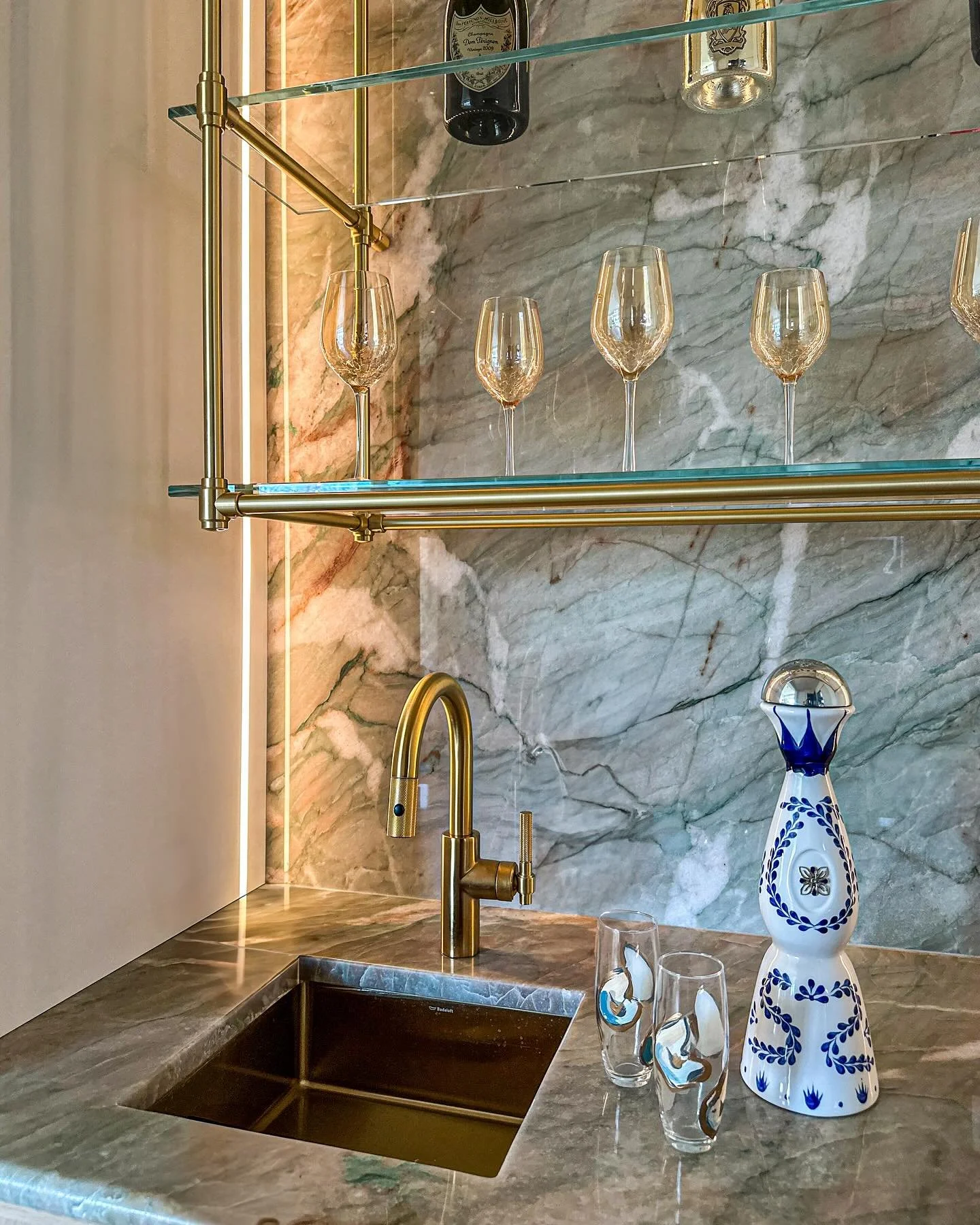 Friday night in, but make it luxe ✨ 

This custom wet bar stuns with dramatic quartzite, ceiling-mounted brass and glass shelves, oak cabinetry with brass inserts, and a gleaming brass sink + faucet. 

Cheers to effortless elegance at home! 🥂 

#dar