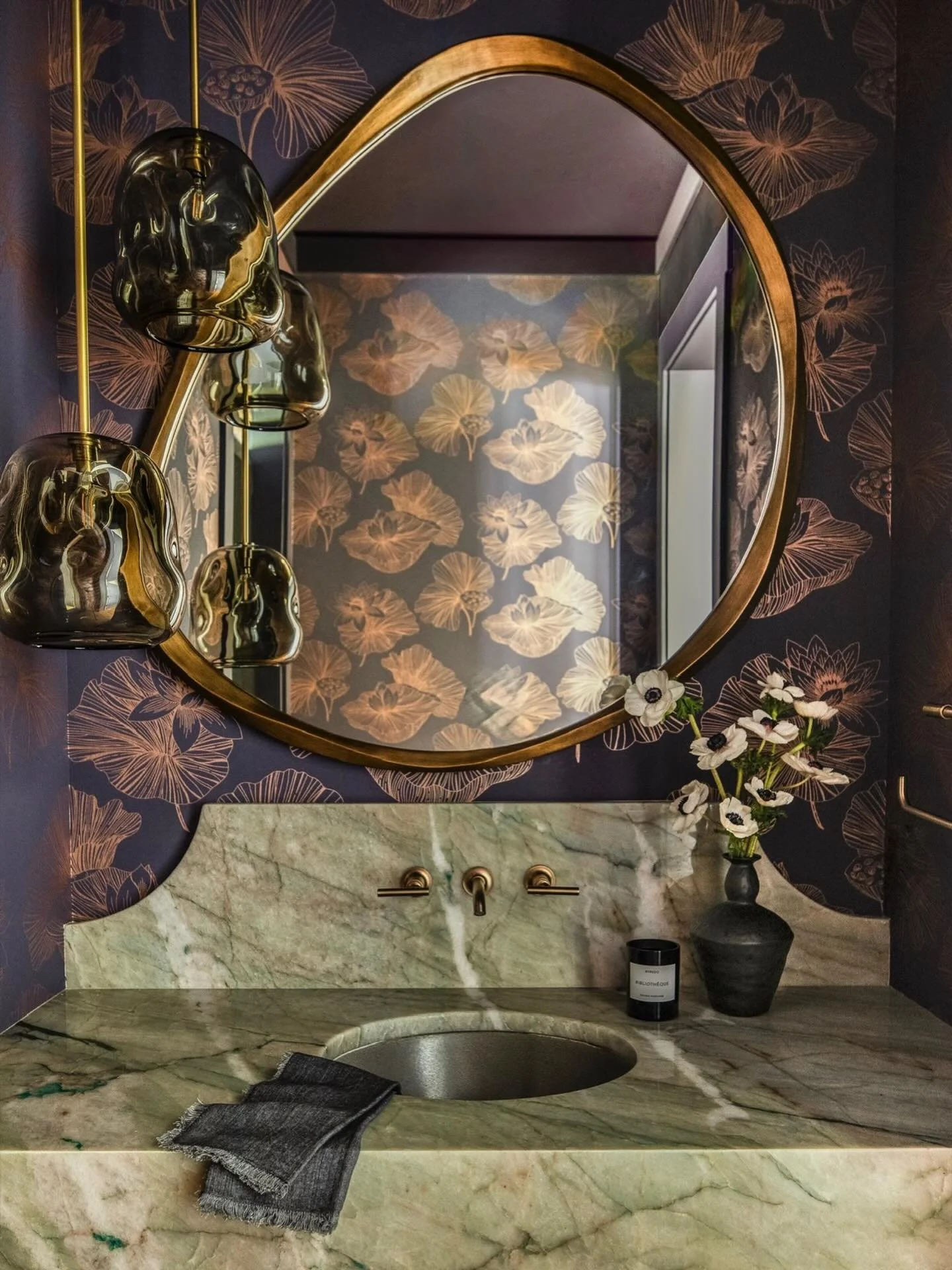 A jewel-box powder room layered in mood and movement. Deep floral walls, sculptural glass pendants, and a floating stone vanity come together to create a space that feels both dramatic and intimate. Every detail was designed to turn a fleeting moment