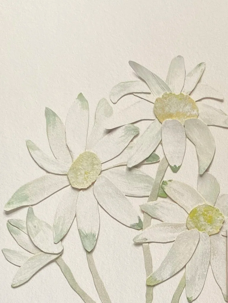Handmade paper flowers resembling daisies with white petals and yellow centers on a white background.