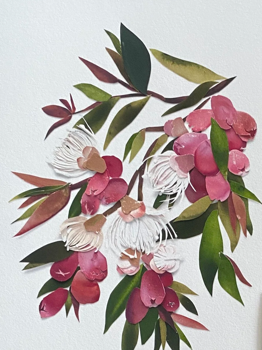 Paper art depicting pink and white flowers with green and reddish leaves on a white background.