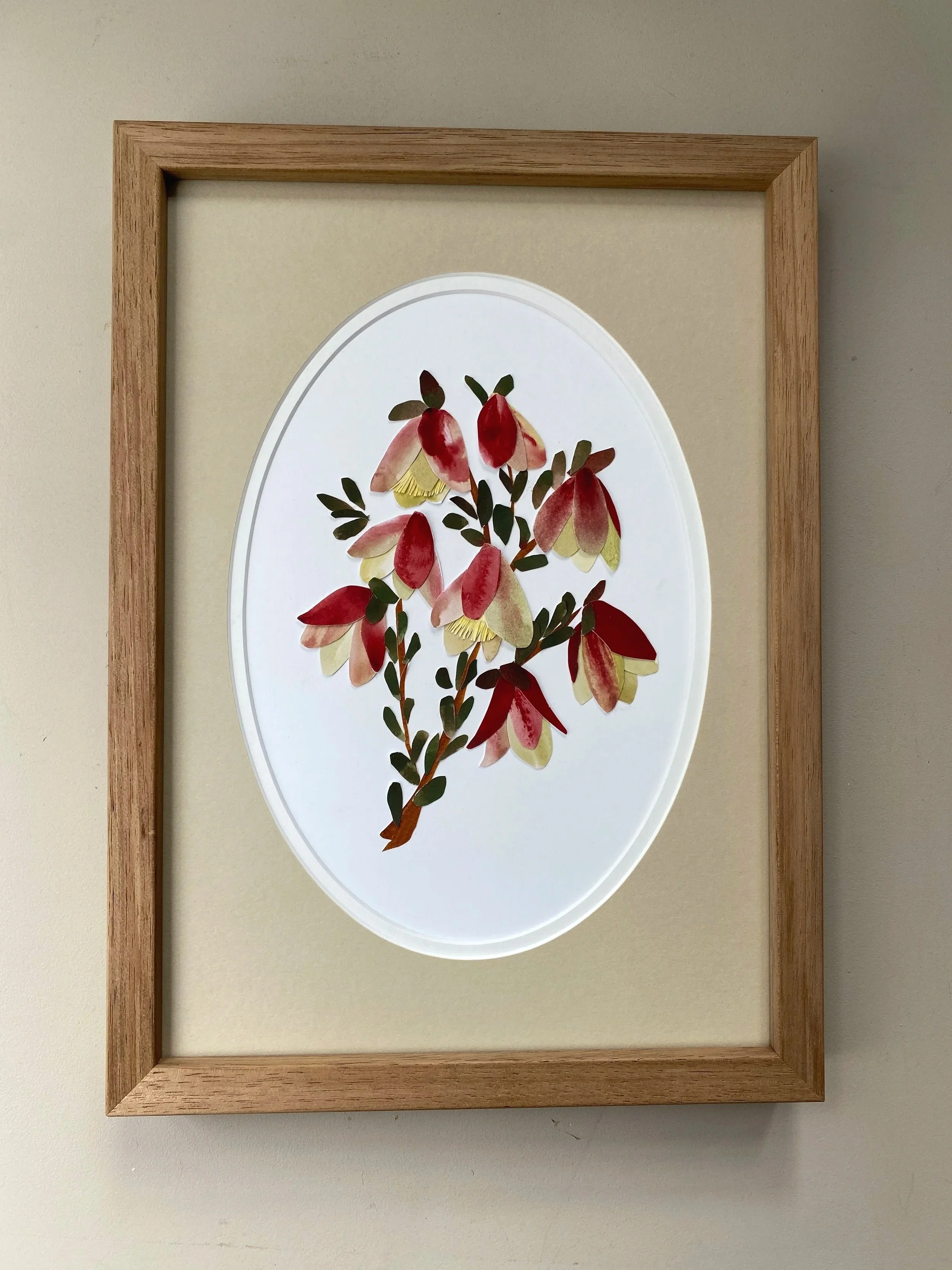 Pressed flower artwork featuring red and cream-colored flowers with green leaves, framed in wood.