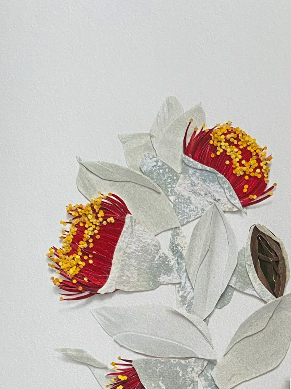 Artificial flower arrangement with red flowers, yellow stamens, and paper leaves against a white background.