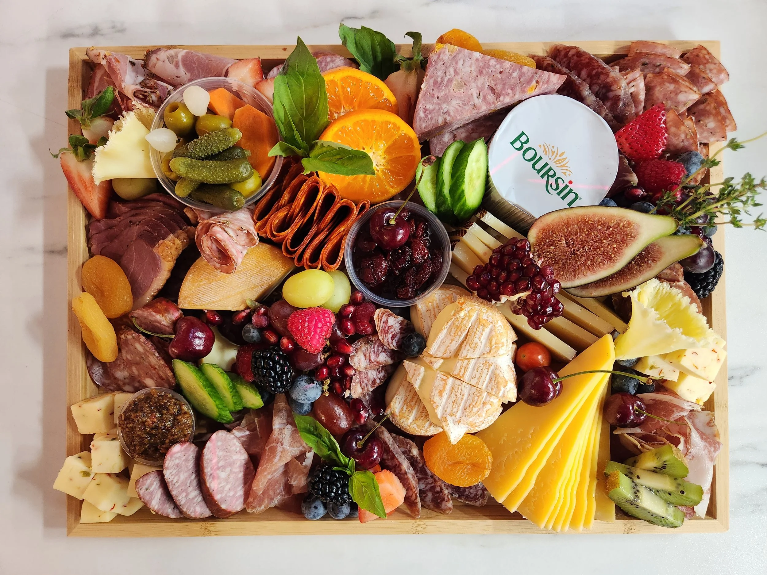 A wooden tray filled with assorted meats, cheeses, fruits, vegetables, and condiments suitable for a charcuterie board.