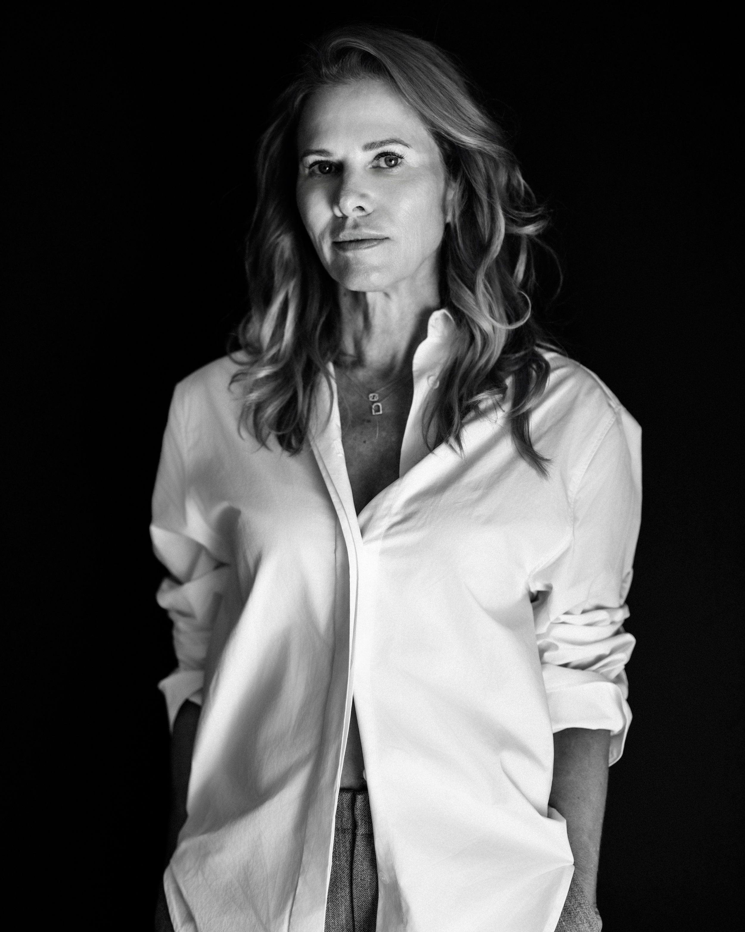 Black and white portrait of a woman with wavy hair, wearing a white shirt with the top button undone, against a dark background.
