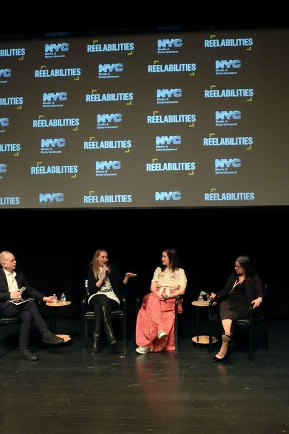 A panel of four, the reelabilities and DOC NYC logos behind on a large screen. From left to right: Kinema's Christie Marchese, The Film Collaborative's Kathy Susca, WMM's Kendra Hodgson, & Reelabilities' Isaac Zablocki