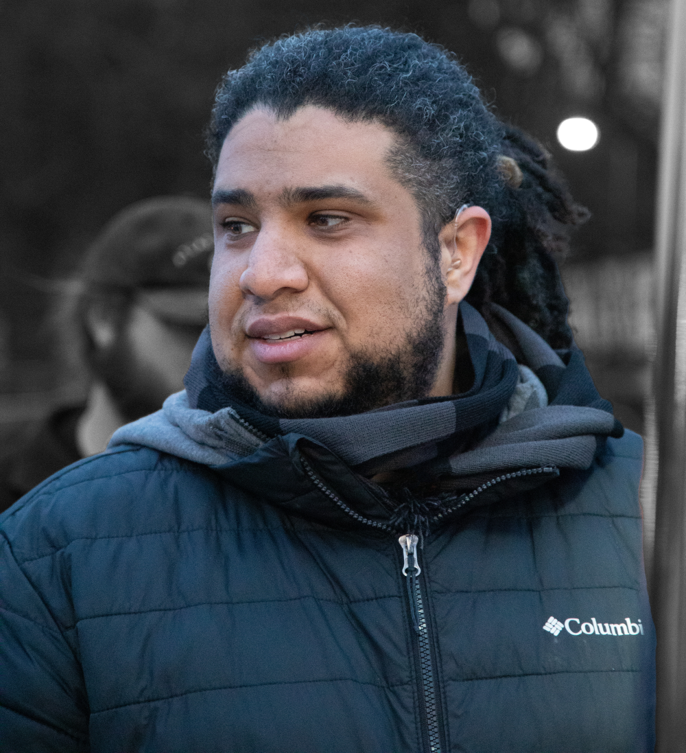 Gabo is an Afro-Venezuelan man with dreadlocks pulled back, a beard, and a fully-zipped winter coat.