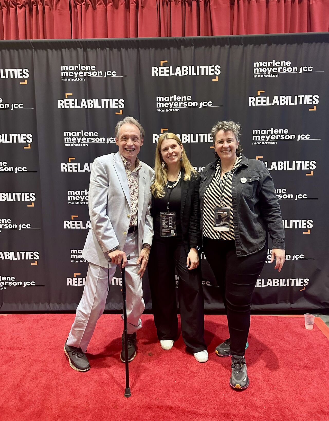 In front of the ReelAbilities NY 2025 step and repeat on a red carpet, Lawrence Carter Long, Sarah Napoli and Cassidy DImon smile.