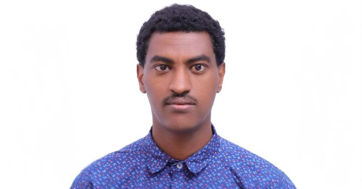 Aschalew Chechebo is a brown-skinned Ethiopian man with short curly hair, a moustache and a patterned blue button-up against a white background.