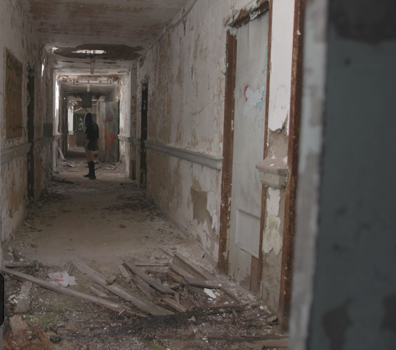 A person stands in an old institutional building that is falling apart.
