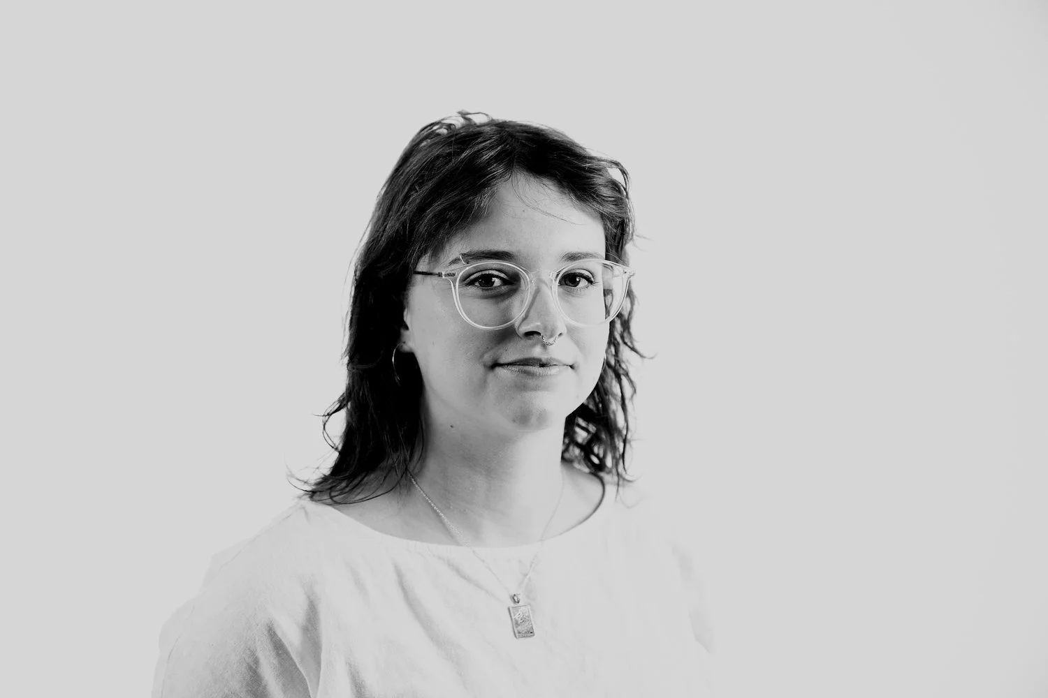 In black and white, Andie is a woman with wavy, dark, layered hair and light-colored glasses in front of a blank background.