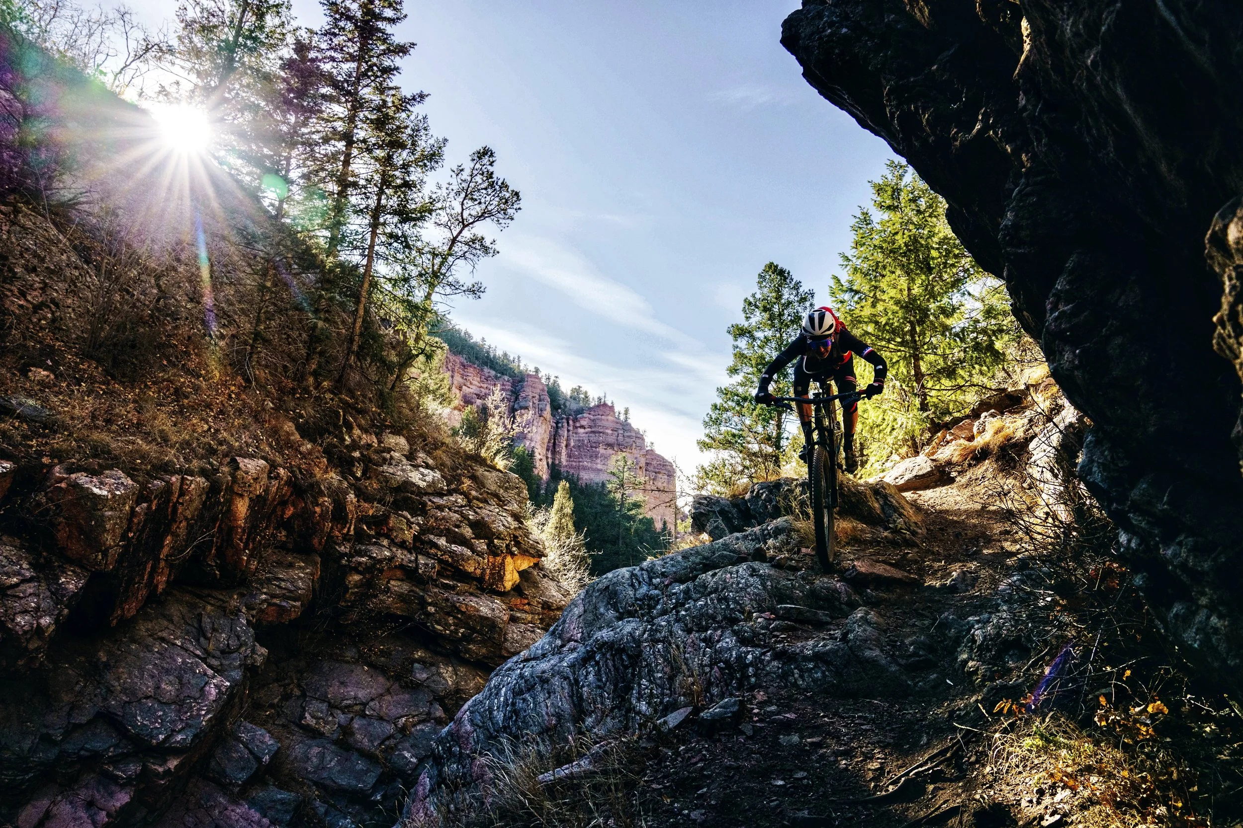 Nick a professional cyclist and mountain biker riding on a rocky trail in a forested canyon with sunlight shining through trees.