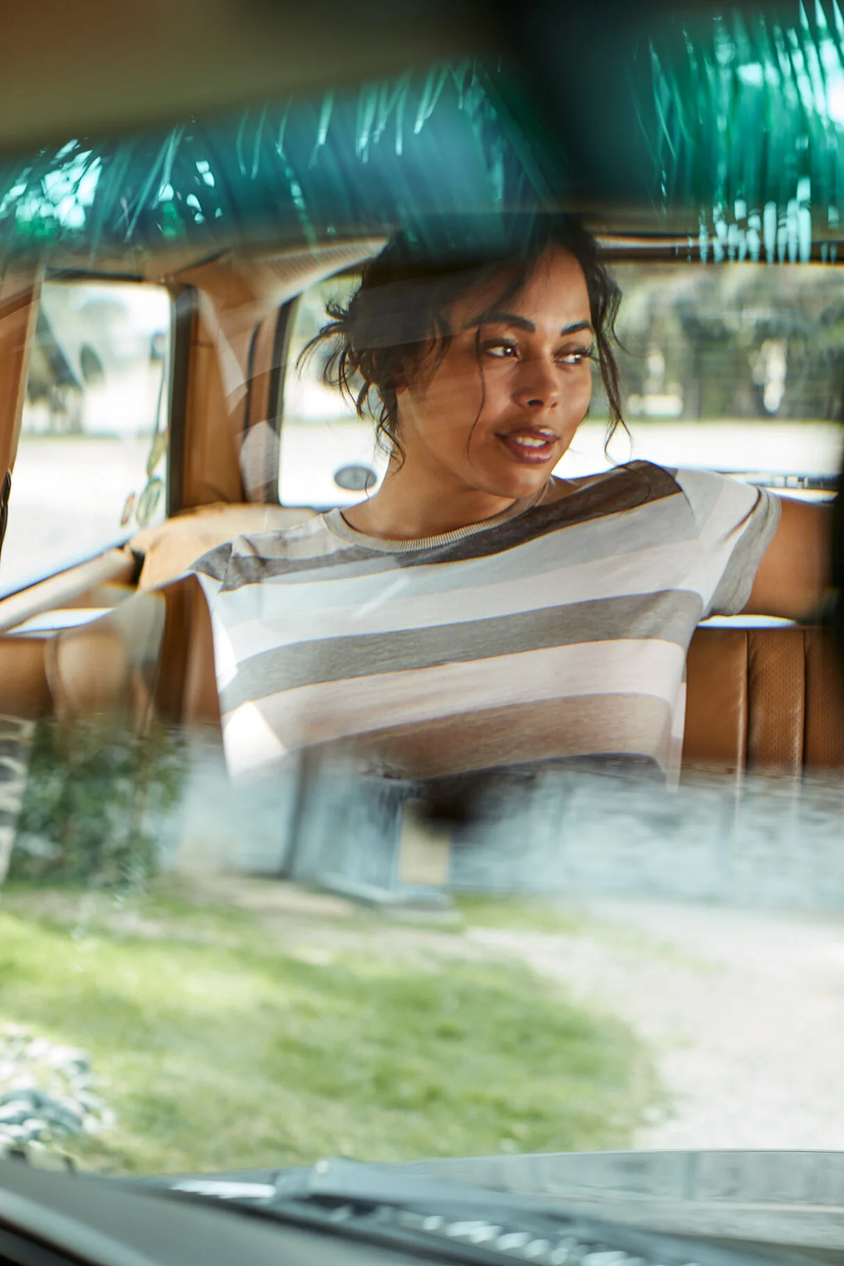 A woman sitting in the backseat of a vehicle, looking out the window with a relaxed expression, wearing a striped t-shirt.
