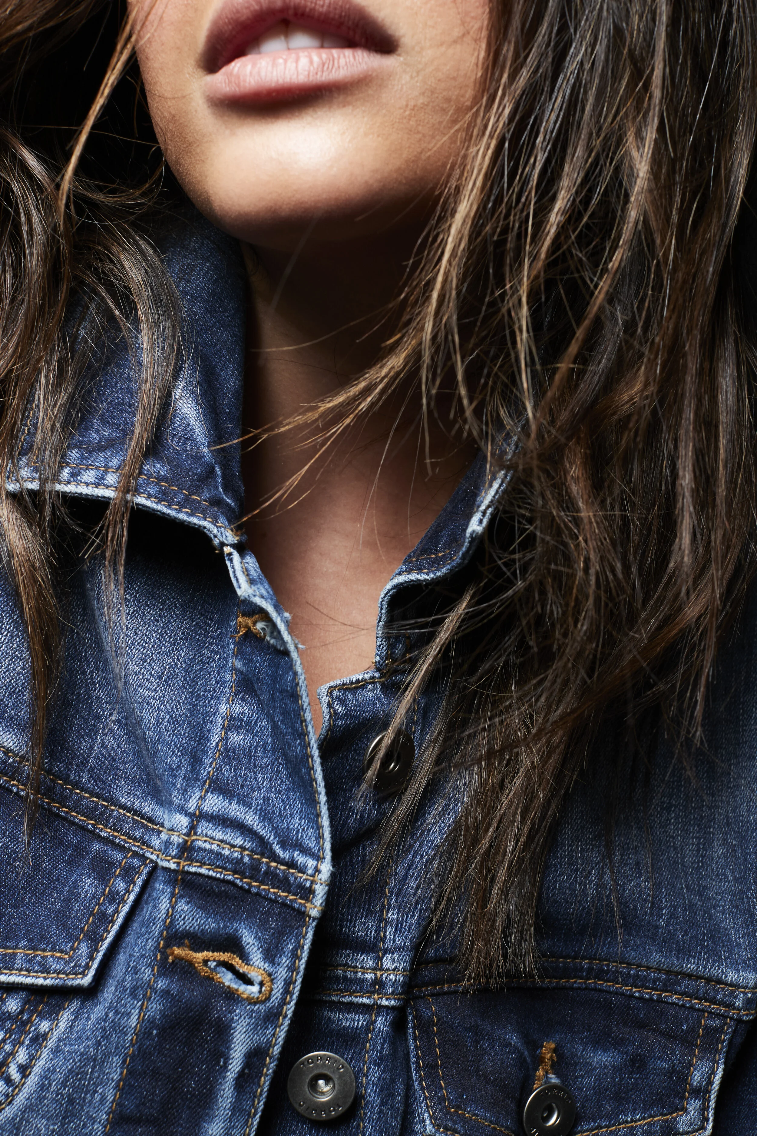 Close-up of a woman wearing a denim jacket, with brown hair and parted lips.