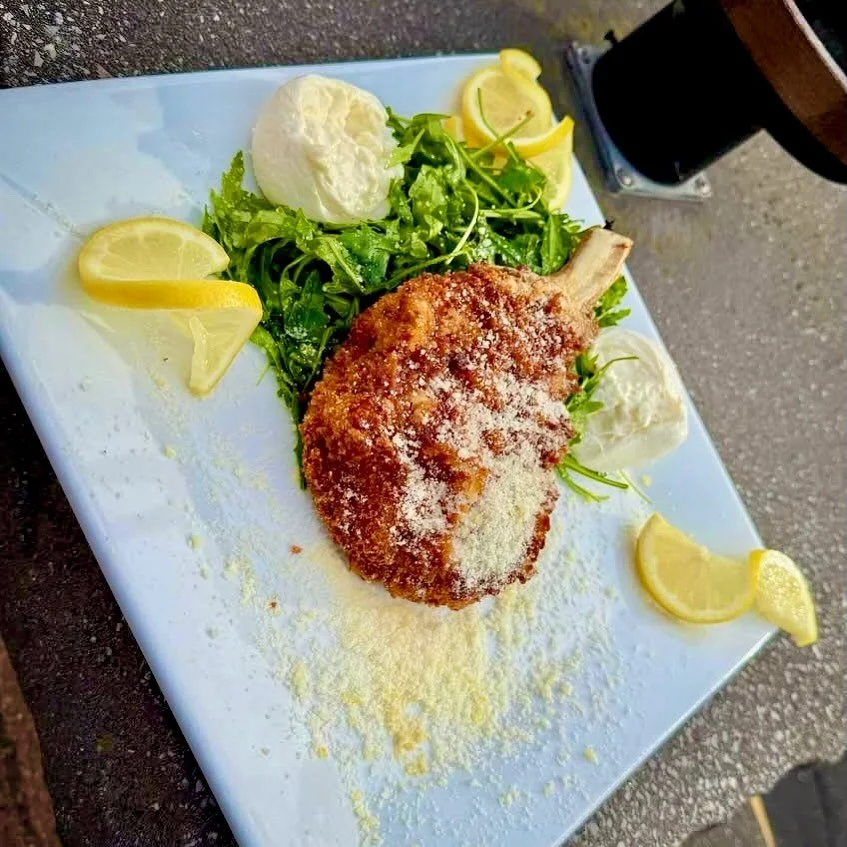 Mayday Milanese- 12 oz center cut pork chop panko encrusted and fried to golden brown. Served with a lightly dressed lemon arugula salad. Finished with shaved parmesan and fresh burrata cheese