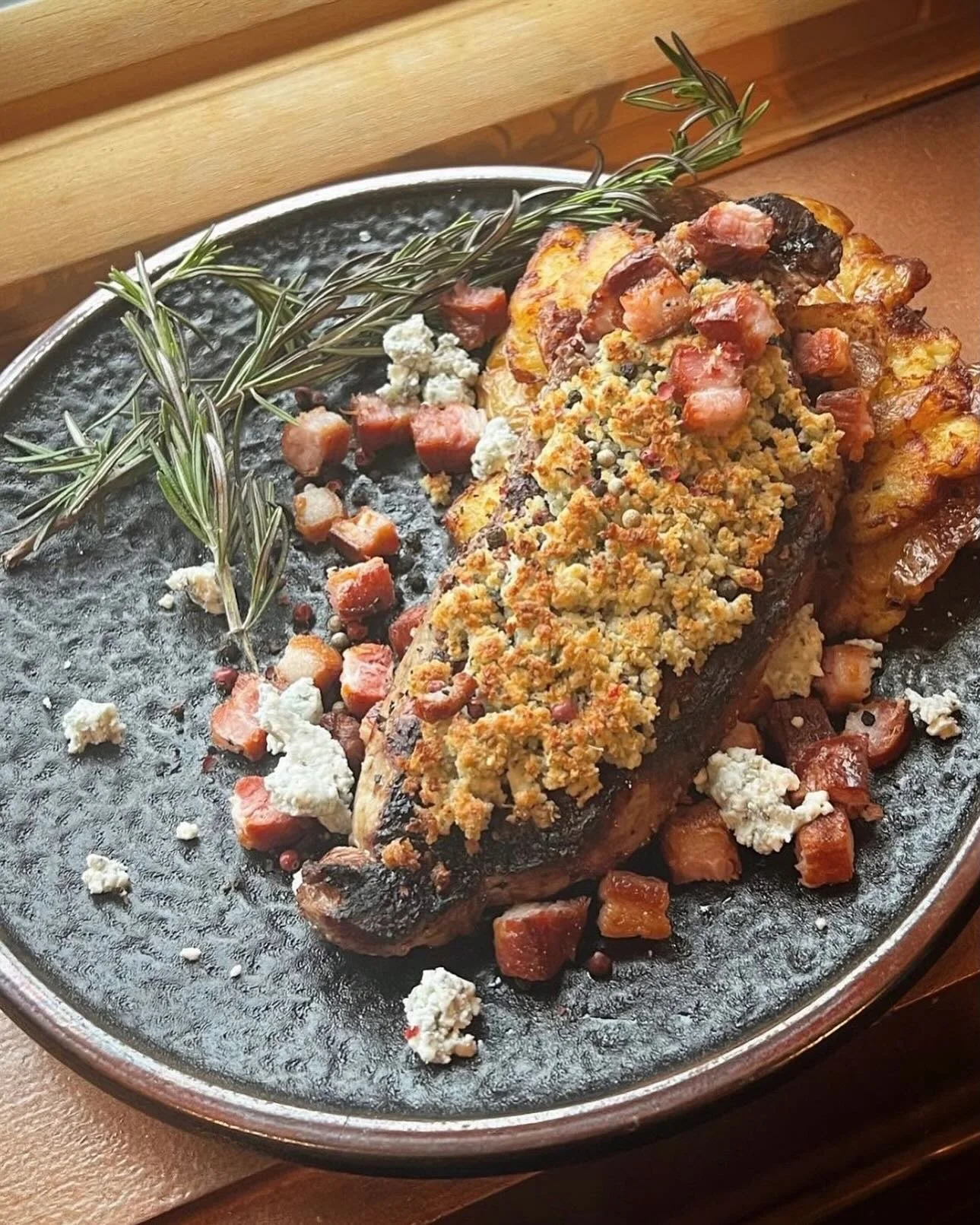 Bacon Blue NY Strip- 12 oz center cut chairman reserve New York strip grilled and topped with a blue cheese crust. Served over golden Yukon smashed potatoes with crispy grilled slab bacon and smoked peppercorns