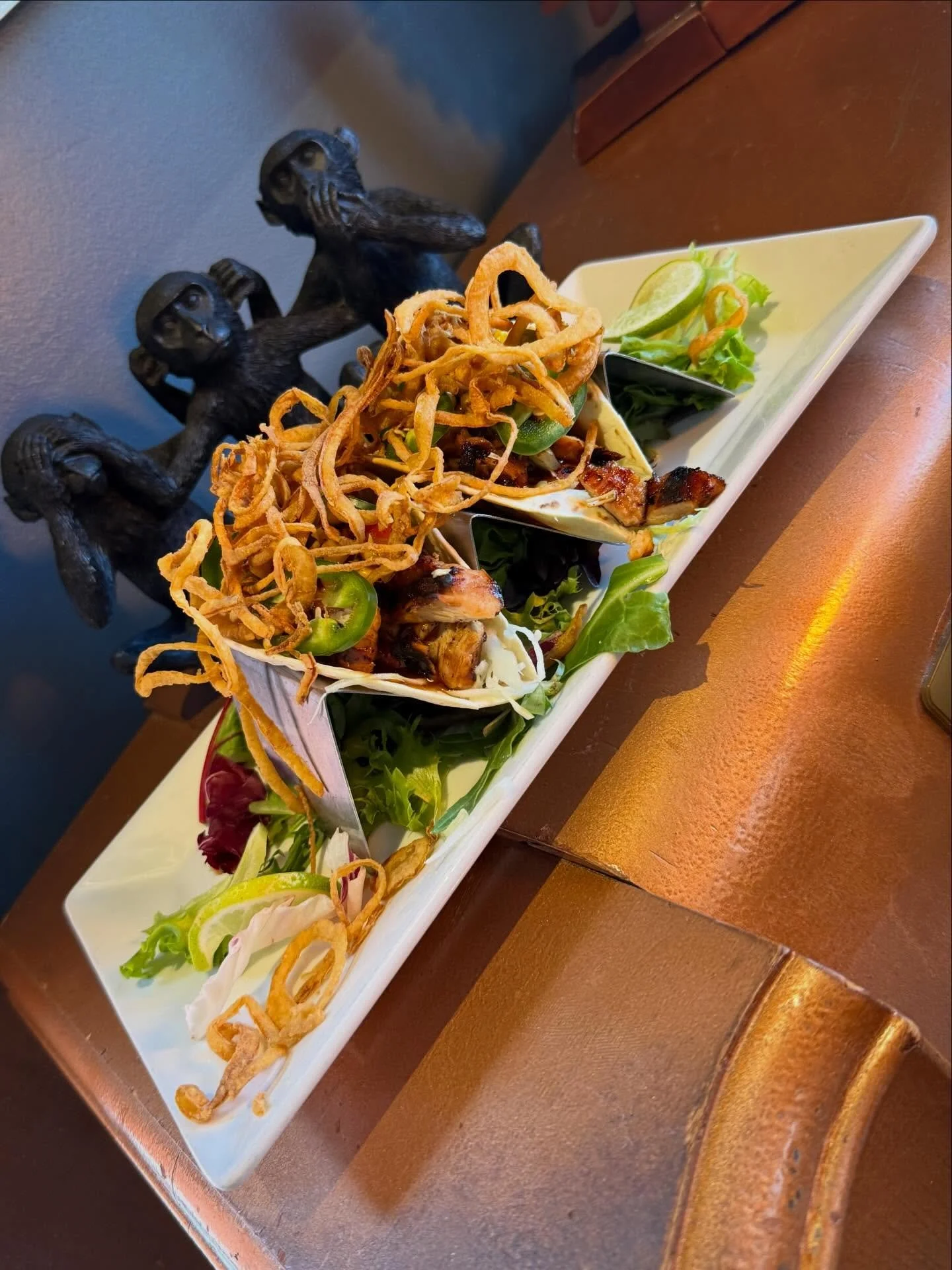 Bourbon Chicken Tacos- Two flour tortillas with bourbon marinaded grilled chicken thighs, topped with shaved cabbage, fire roasted corn, bourbon sauce, sliced jalapenos and finished with crispy onion straws