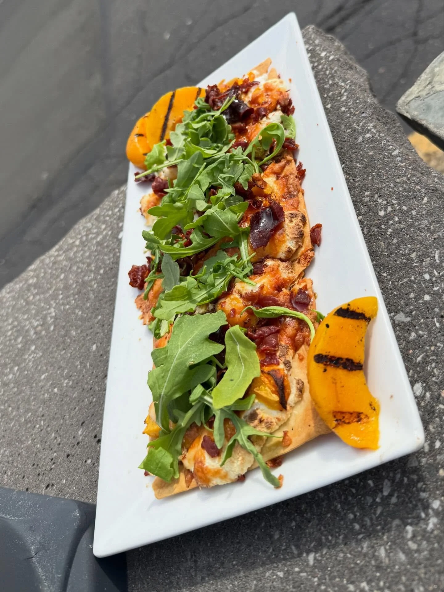 Peach Turbulence- Crispy thin crust flatbread topped with whipped honey ricotta, peaches, Monterey jack cheese, crispy prosciutto, hot honey drizzle, arugula and toasted pistachios