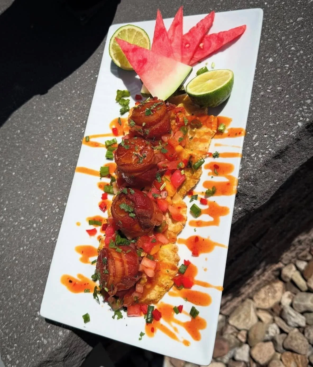 Sweet heat meets island vibes 🌴🔥

Tropical Scallop &amp; Tostones&mdash;bacon-wrapped scallops, perfectly seared with Cajun spice, stacked over crispy fried green plantains. Topped with our house-made tropical pico (watermelon, mango &amp; guava) a