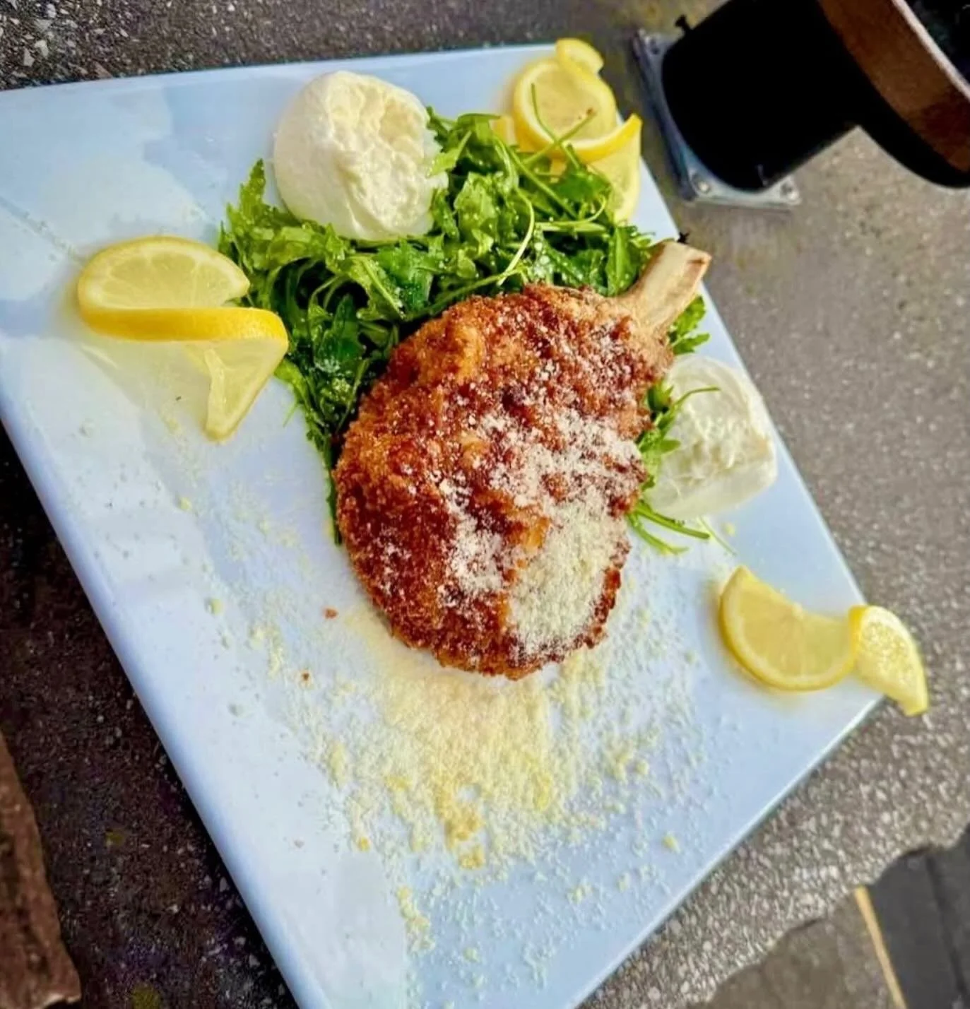 Mayday Milanese- 12 oz center cut pork chop panko encrusted and fried to golden brown. Served with a lightly dressed lemon arugula salad. Finished with shaved parmesan and fresh burrata cheese