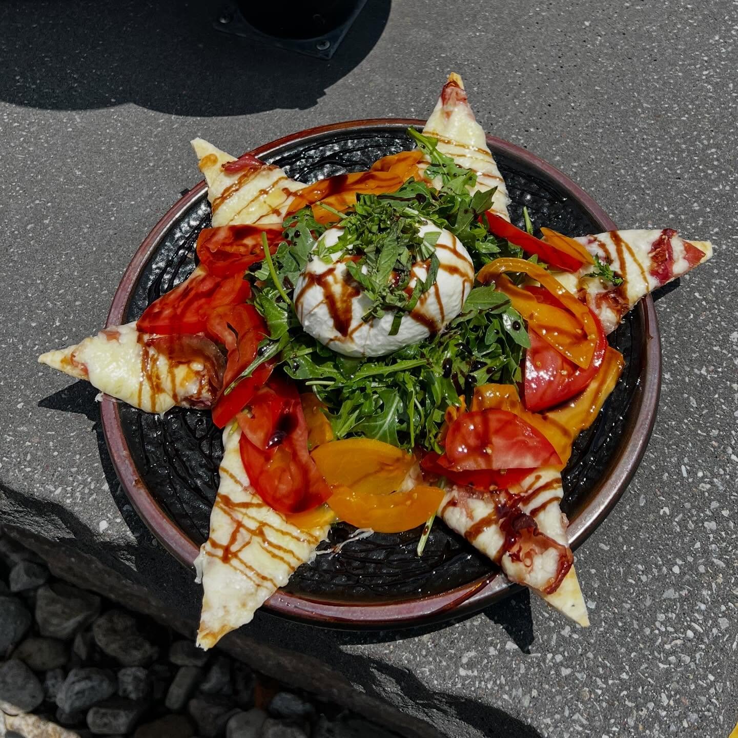 Heirloom Burrata- Crispy thin crust flatbread topped with garlic olive oil, Monterey Jack cheese, with lightly dressed arugula salad, heirloom tomatoes and a whole burrata. Finished with an aged balsamic reduction