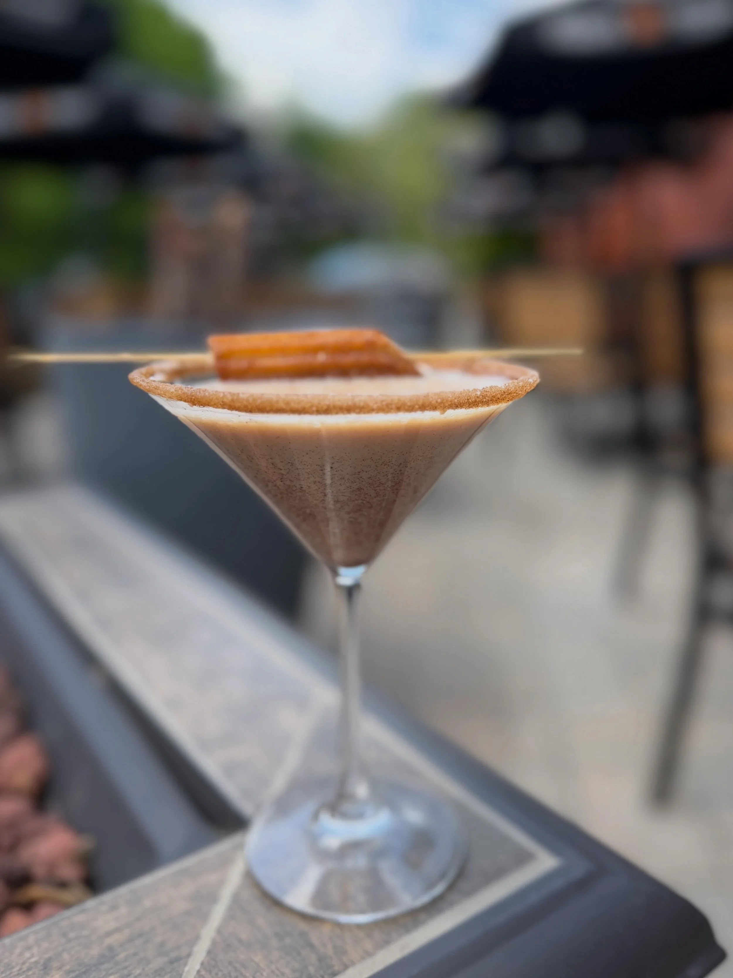 Churro Martini blends smooth vanilla vodka, creamy Baileys, RumChata, and house-made cinnamon simple for the perfect sweet sip. Finished with a cinnamon sugar rim and a mini churro on top. #liquiddessert